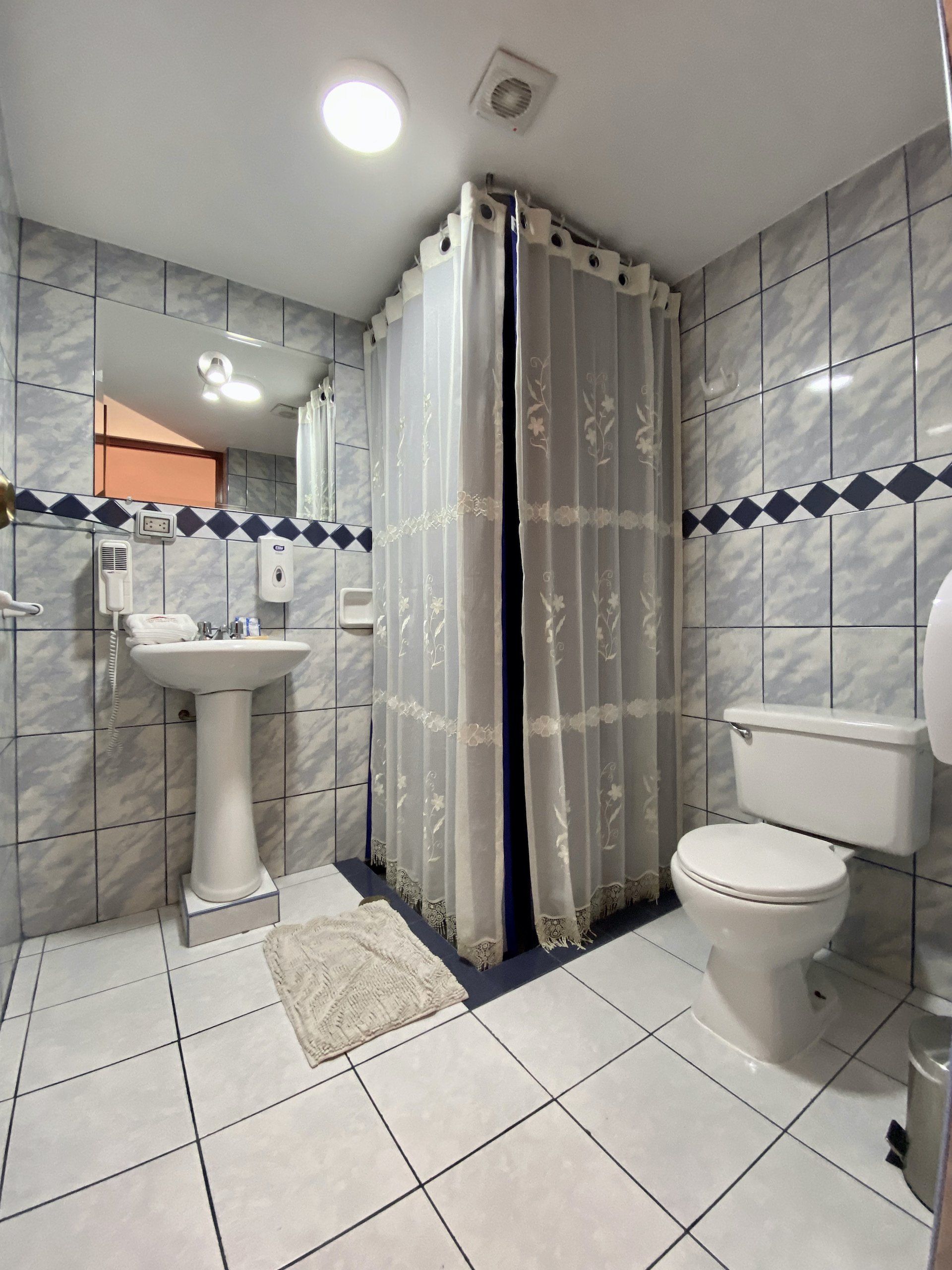 Small tiled bathroom with shower, sink, and toilet, shown from the doorway.