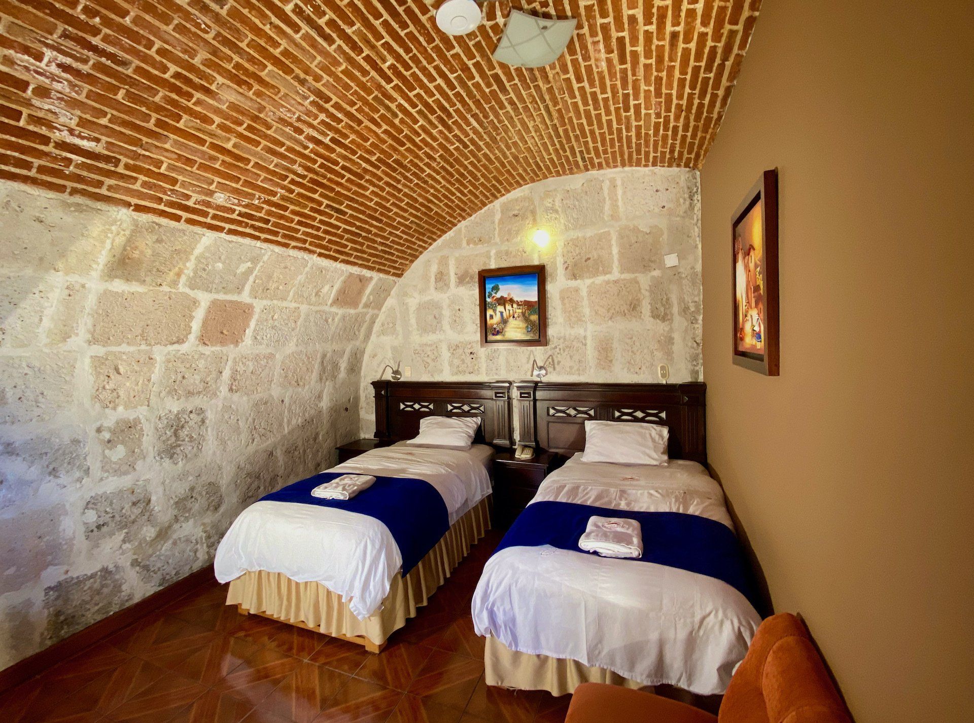 Stone-vaulted bedroom with two twin beds, white and blue bedding, and framed wall art.