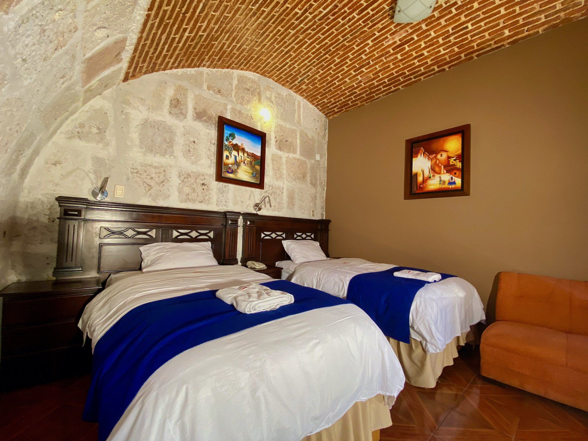 Cozy bedroom with two beds, stone wall, arched brick ceiling, and orange sofa