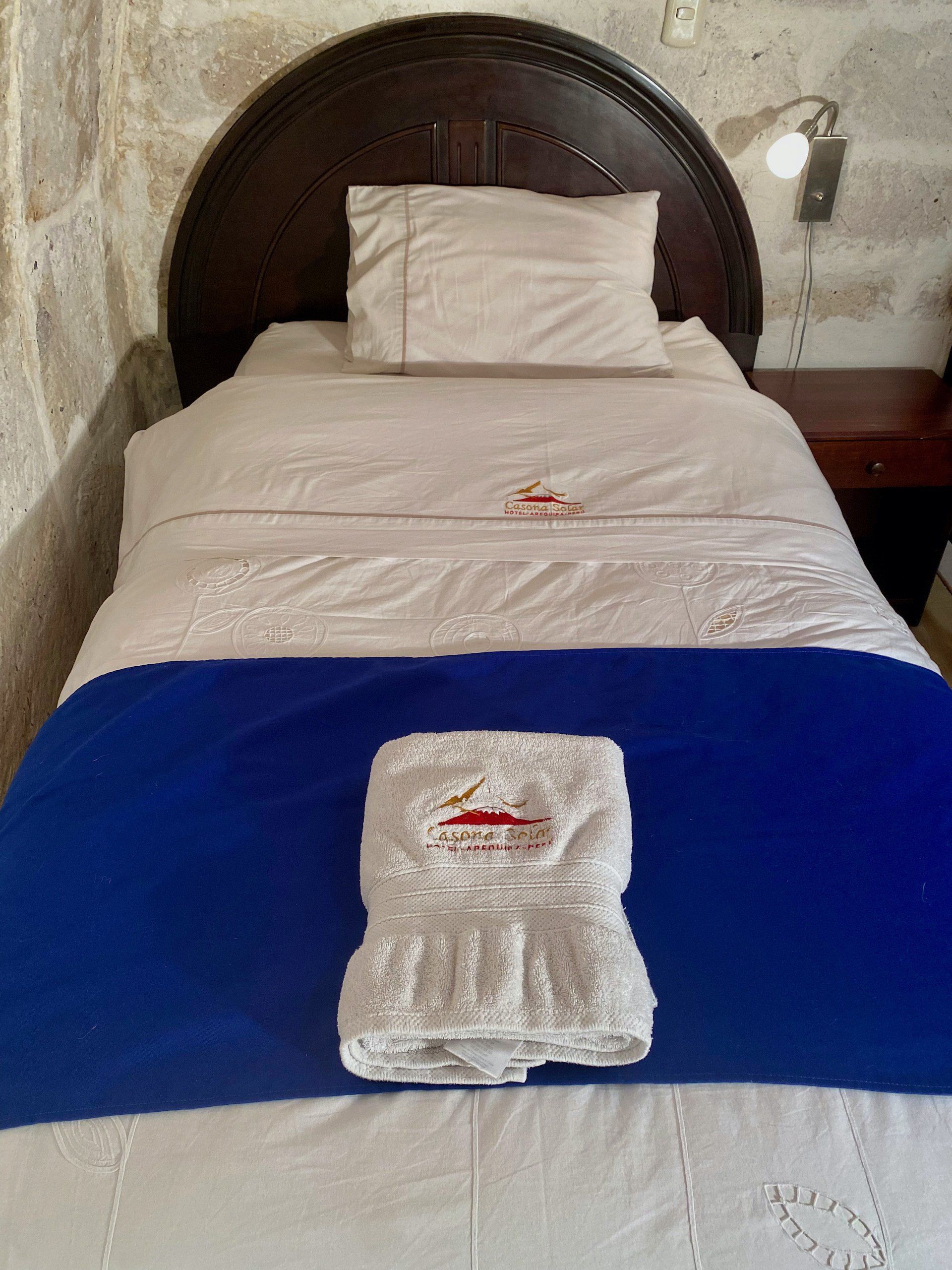 Neatly made bed with white linens, a blue runner, and folded towels in a hotel-style room