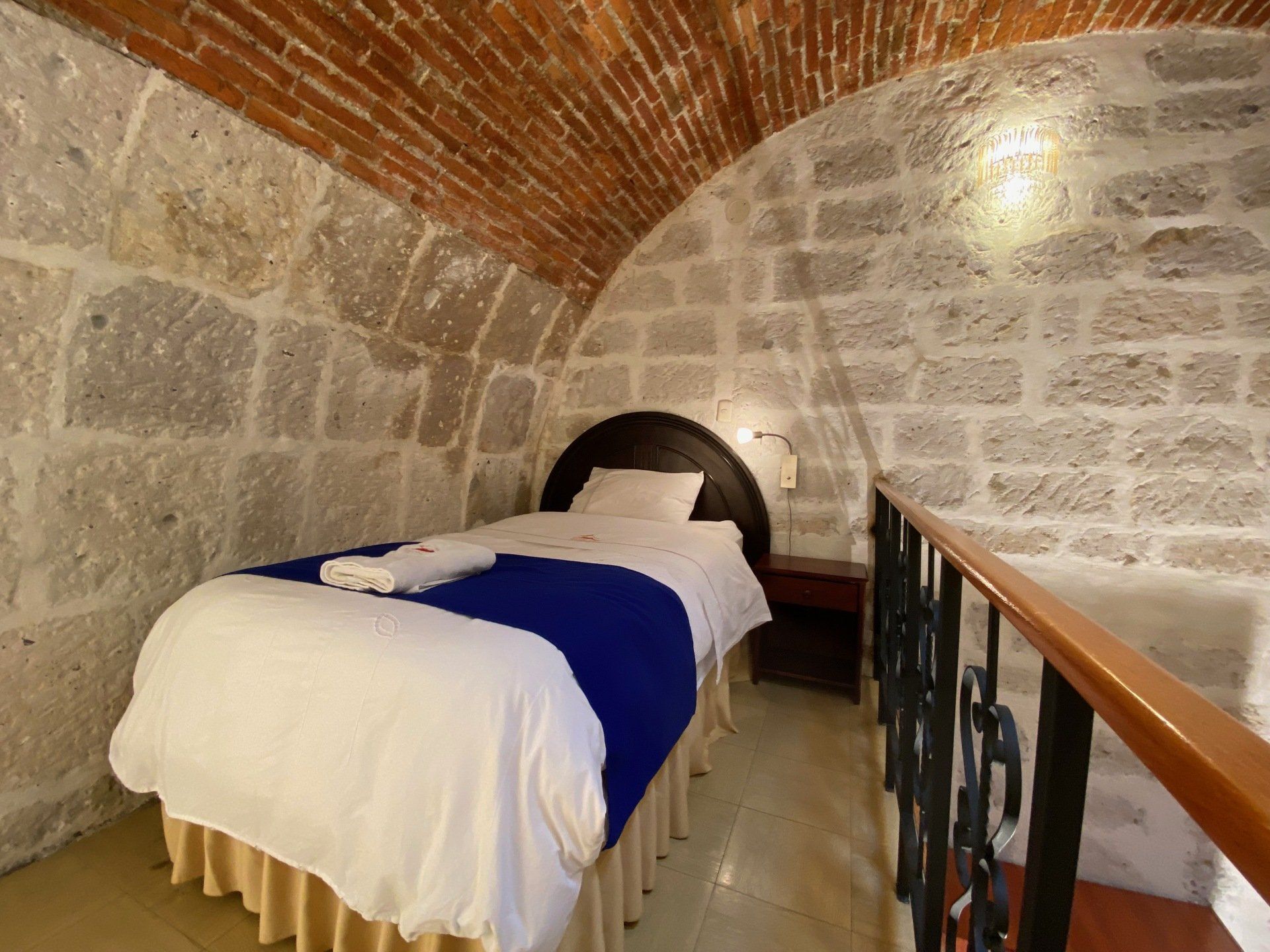 Stone-vaulted bedroom with a single bed, white bedding, and a blue runner in a small alcove room