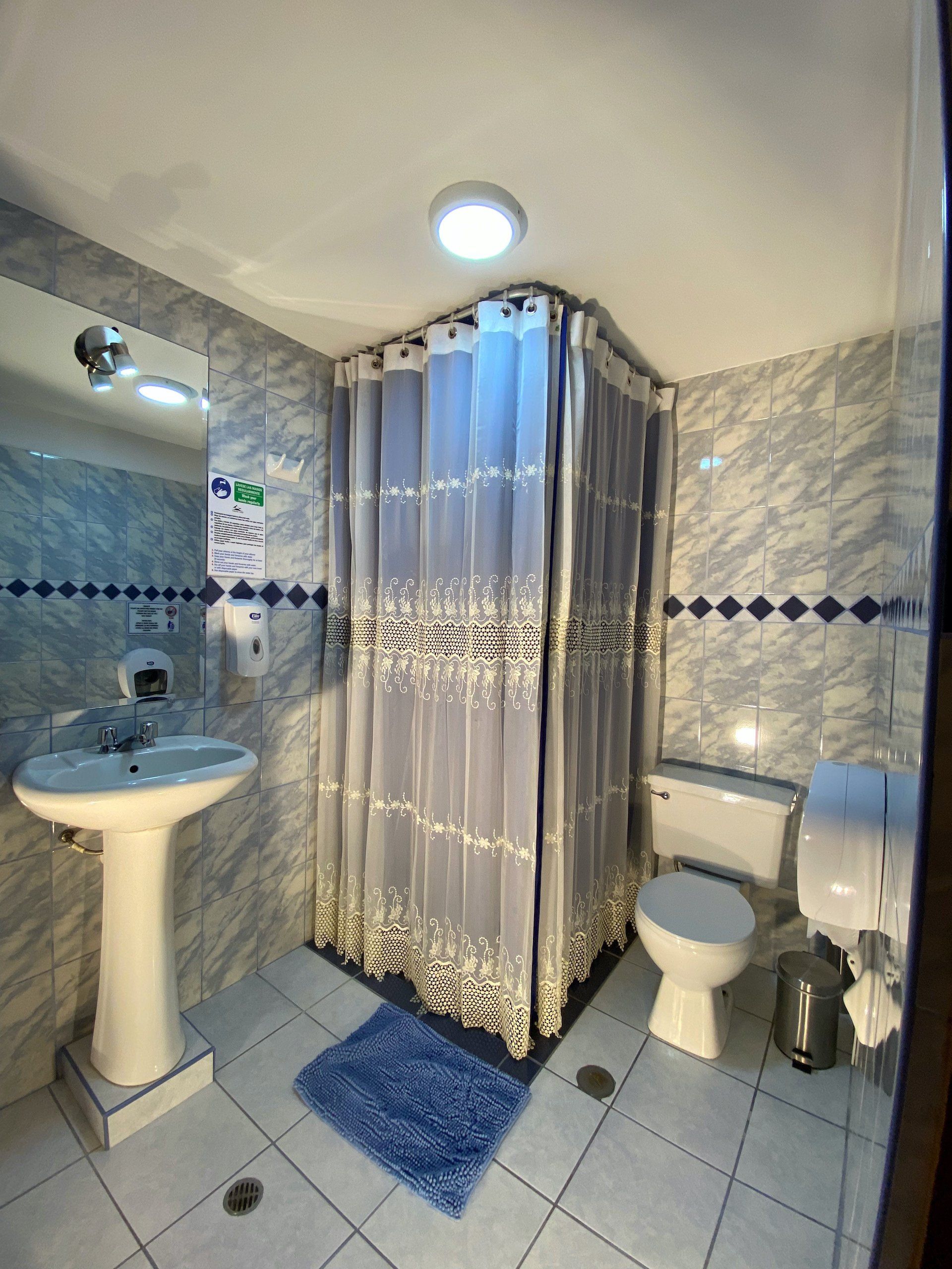 Small bathroom with shower curtain, pedestal sink, toilet, and blue-tiled floor and walls.