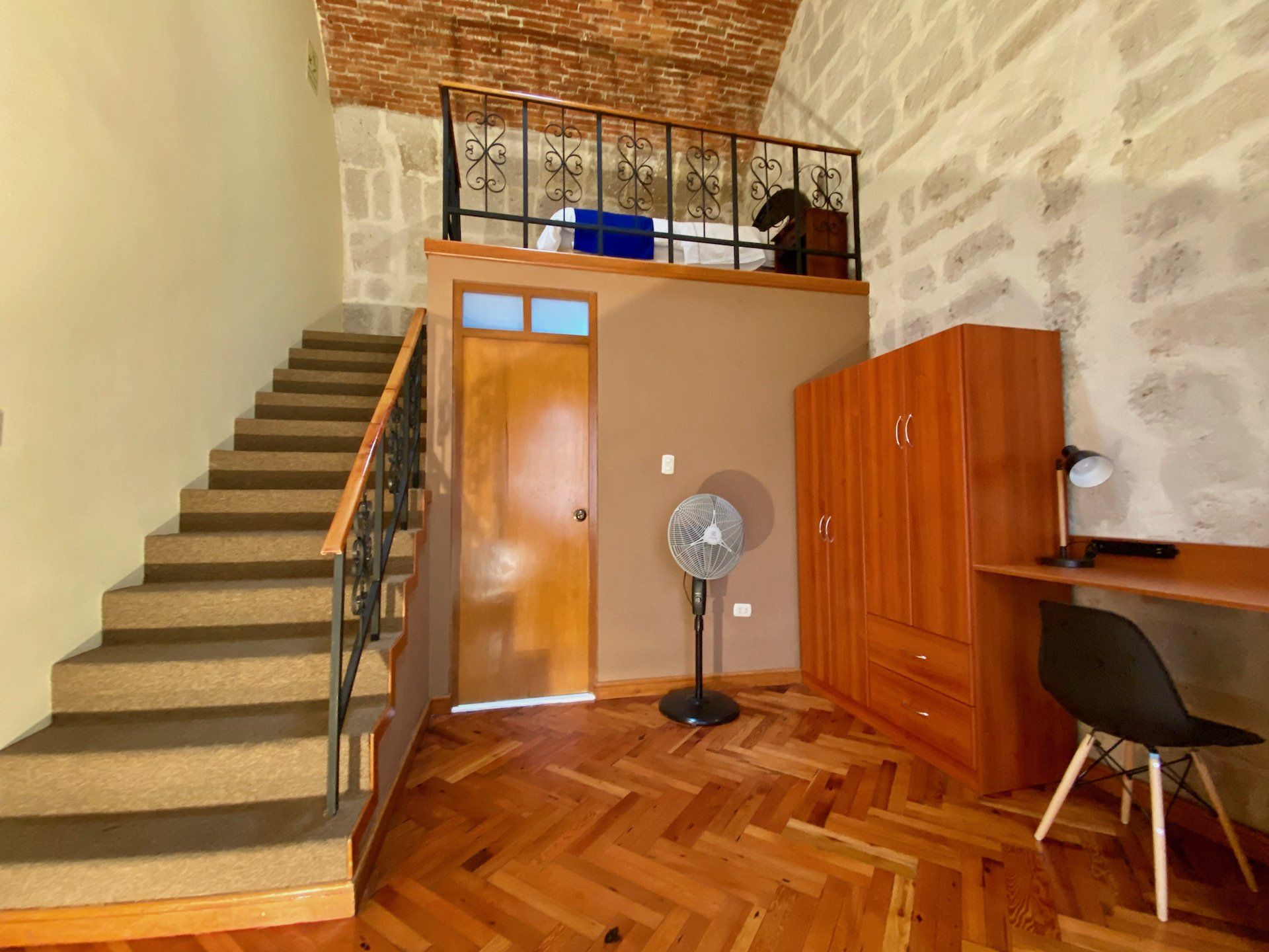 Indoor entry hall with staircase, wooden cabinet, fan, desk, and herringbone wood floor