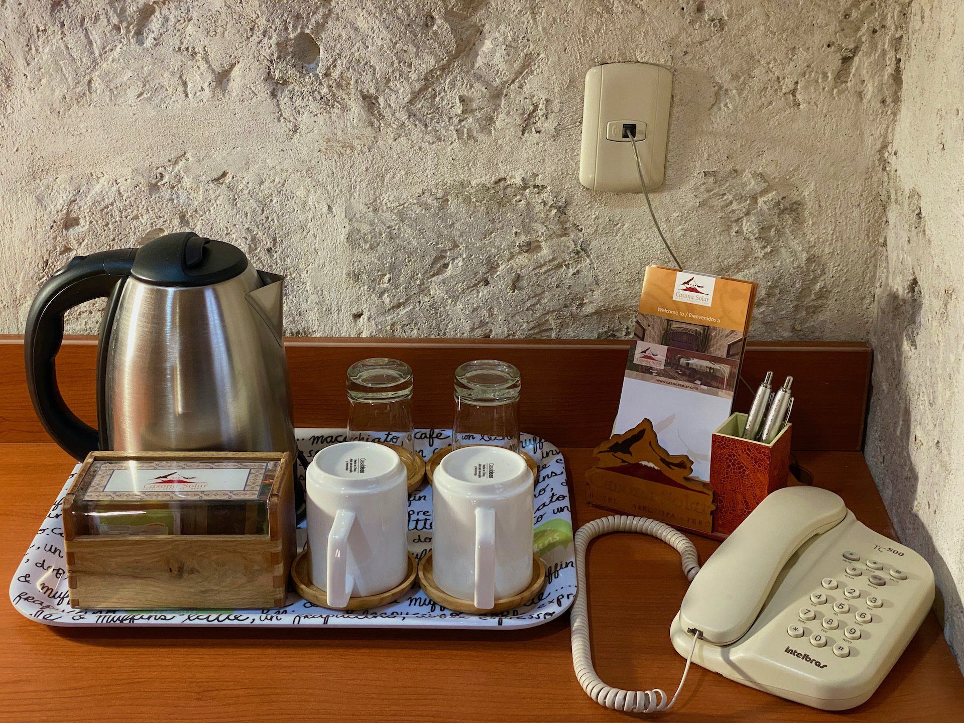 Hotel room tray with kettle, cups, tea packets, and a white telephone on a wooden table