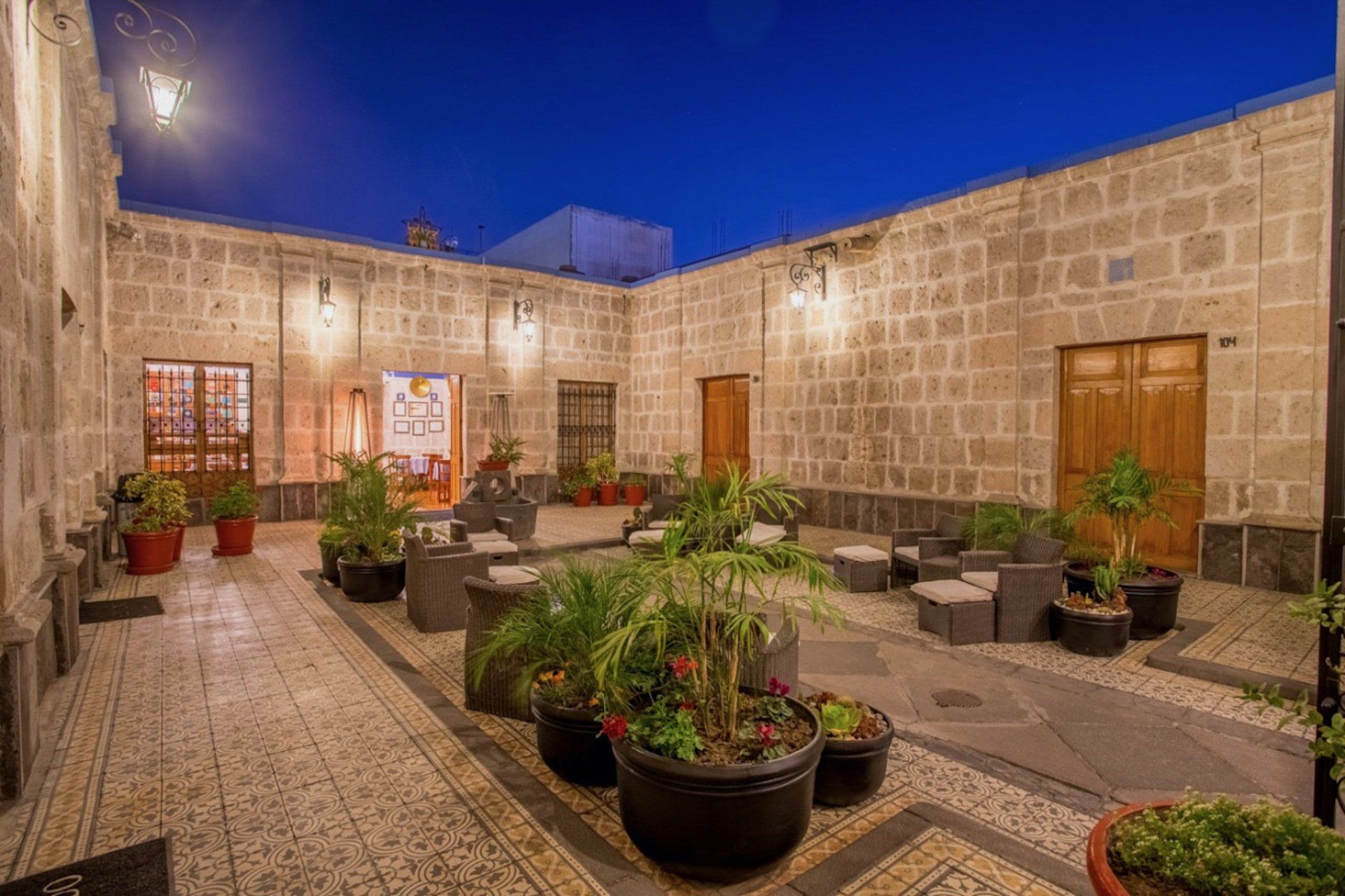 Patio de noche, muros de piedra, plantas en macetas, zona de estar.