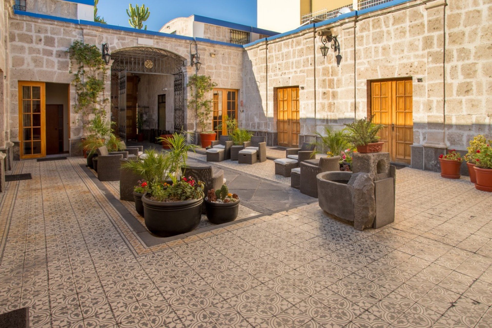 Patio con suelo de baldosas, paredes de piedra, plantas en macetas, zona de estar y puertas de madera.