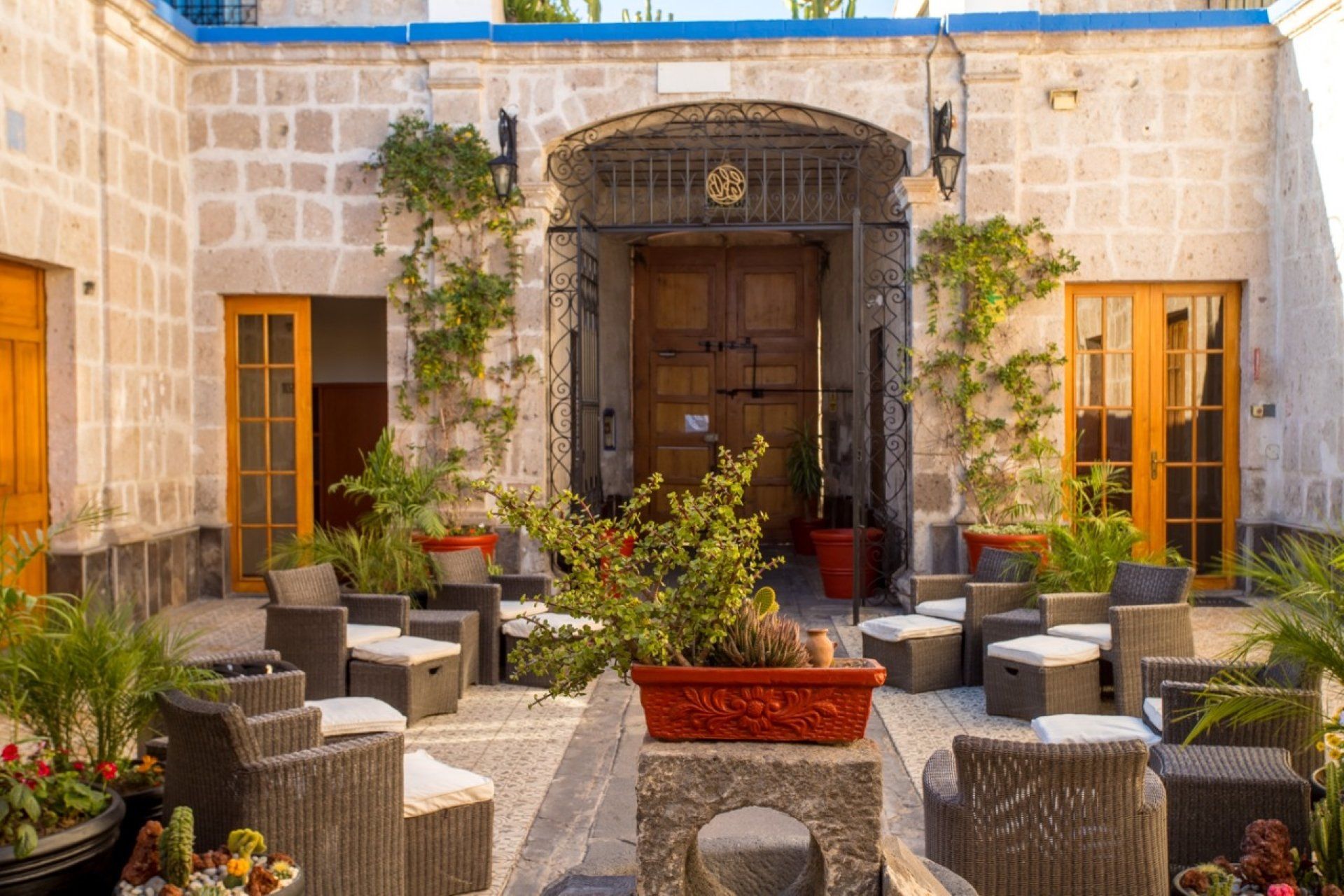 Patio con asientos, plantas y puerta arqueada en un edificio de piedra.