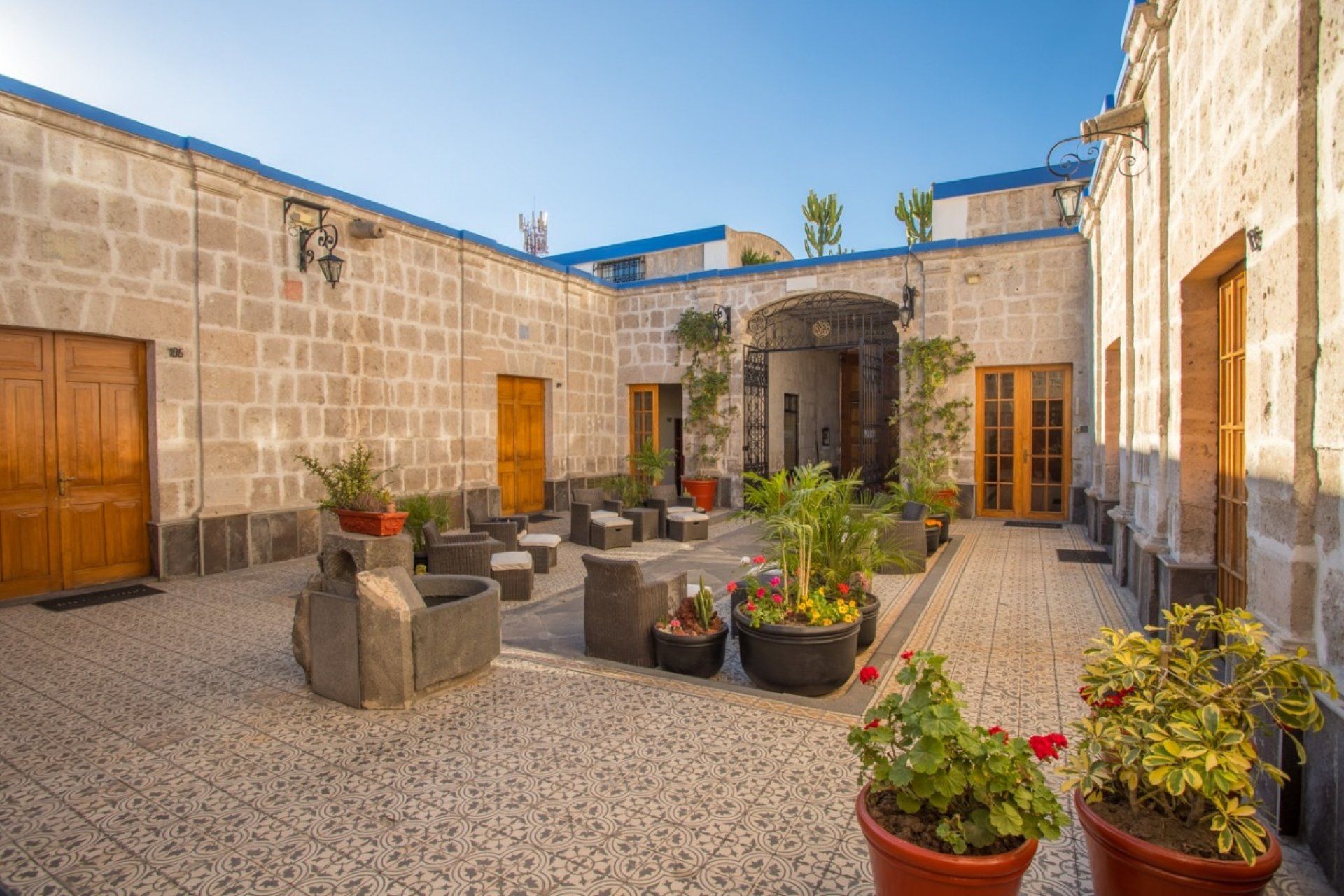 Stone courtyard with potted plants, wooden doors, and a bright blue sky