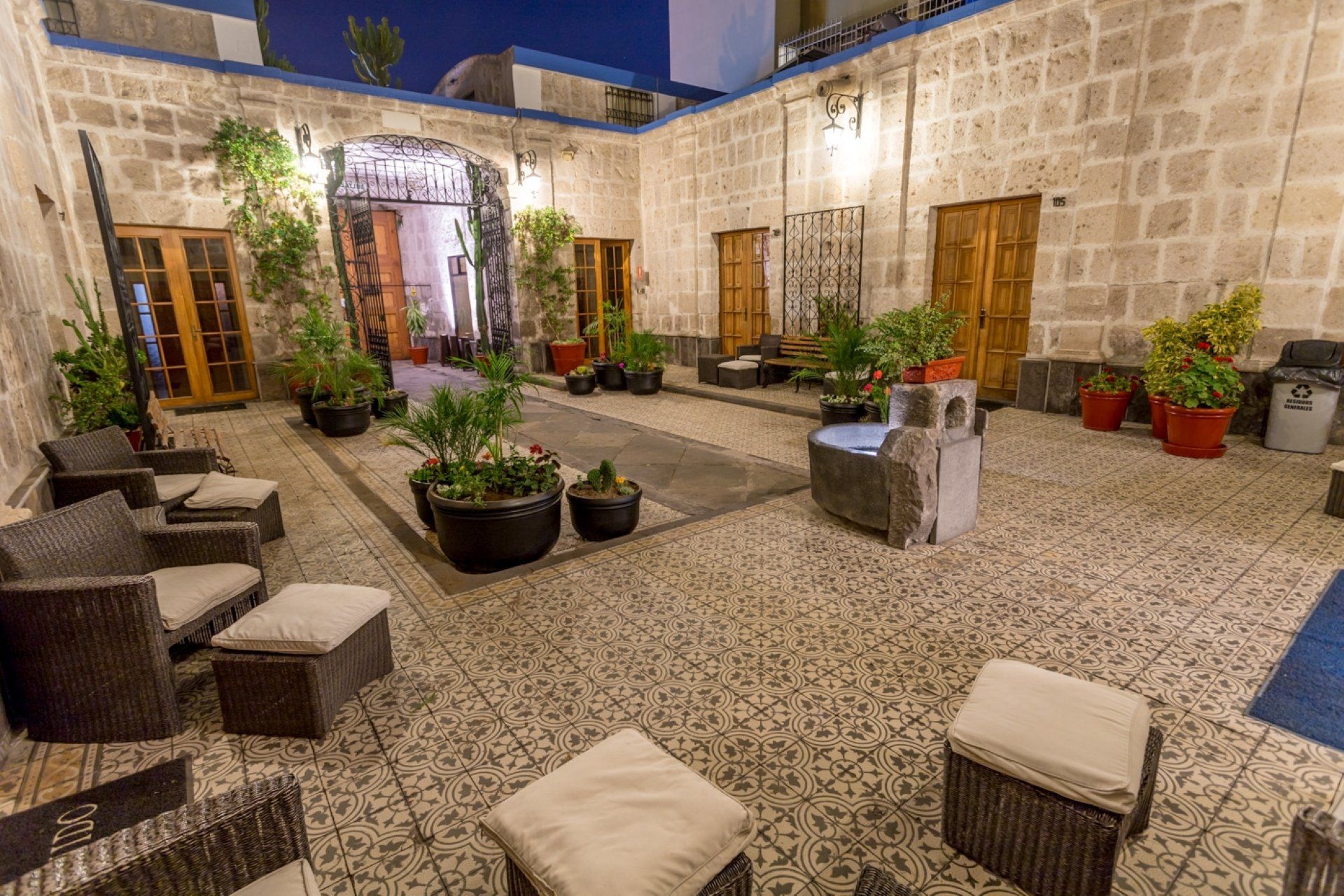 Stone courtyard with potted plants, wicker chairs, and warm evening lighting