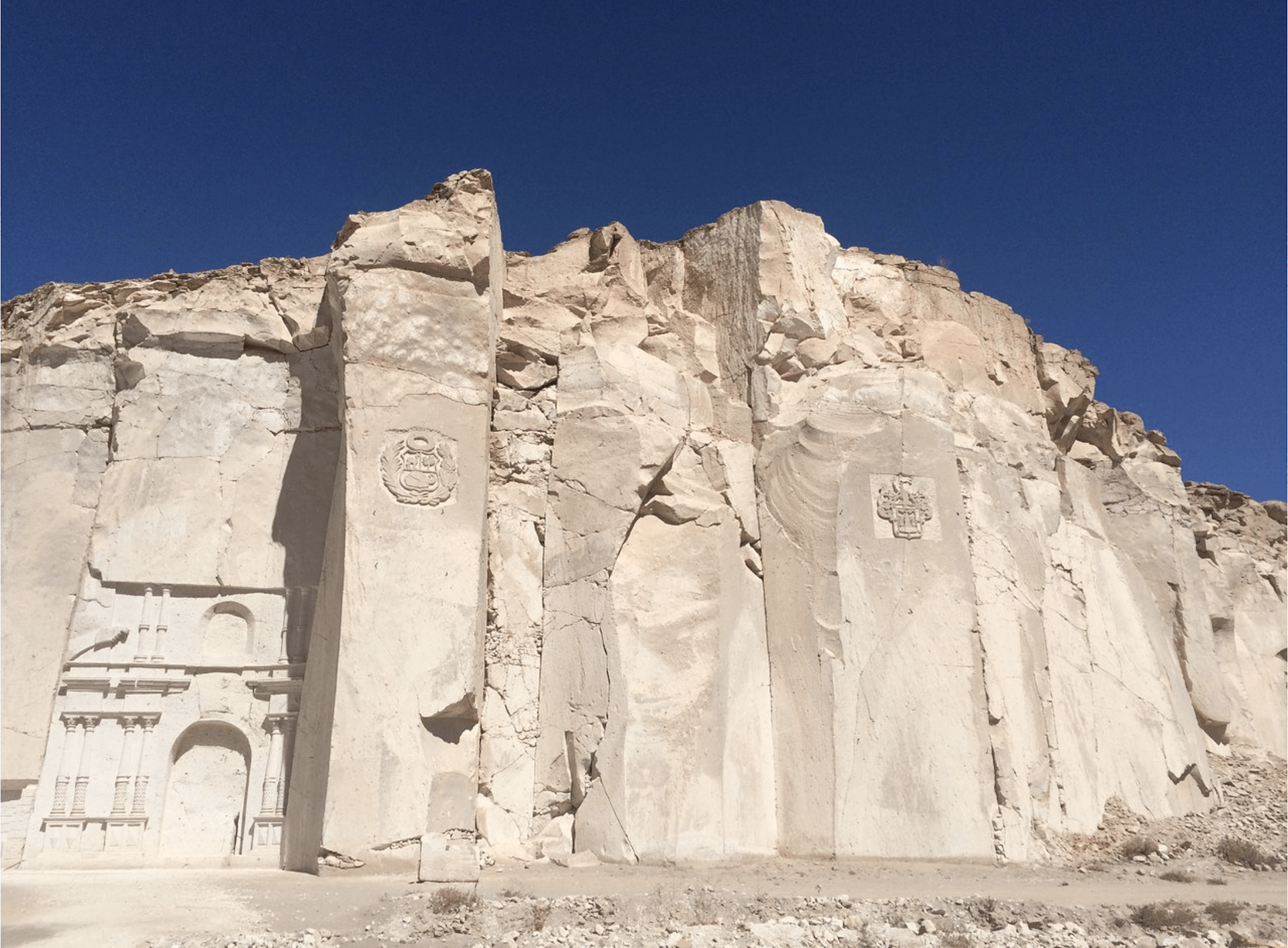 White rock cliff carvings under a clear blue sky in a desert landscape