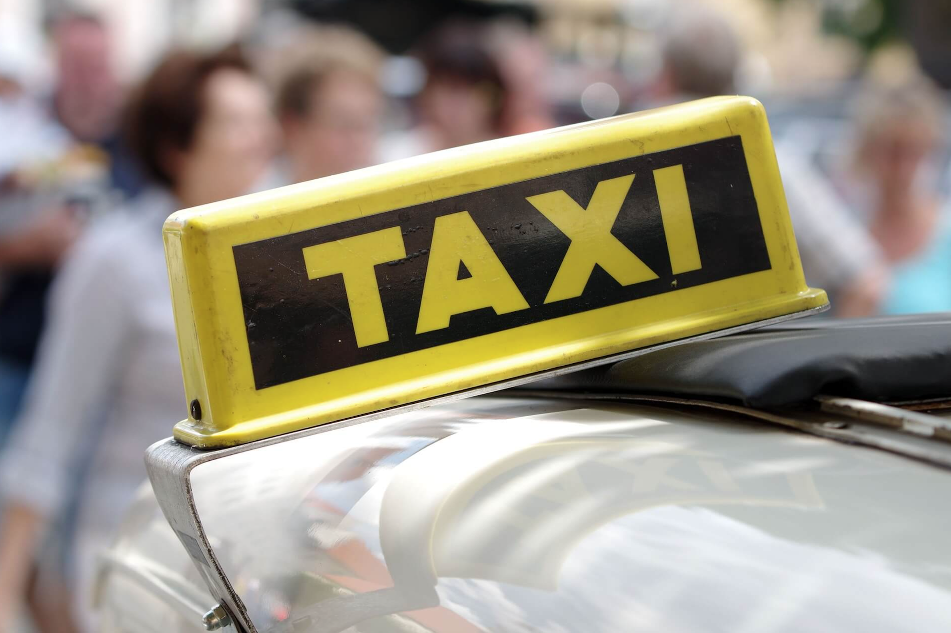 Yellow taxi sign on top of a car with blurred people in the background