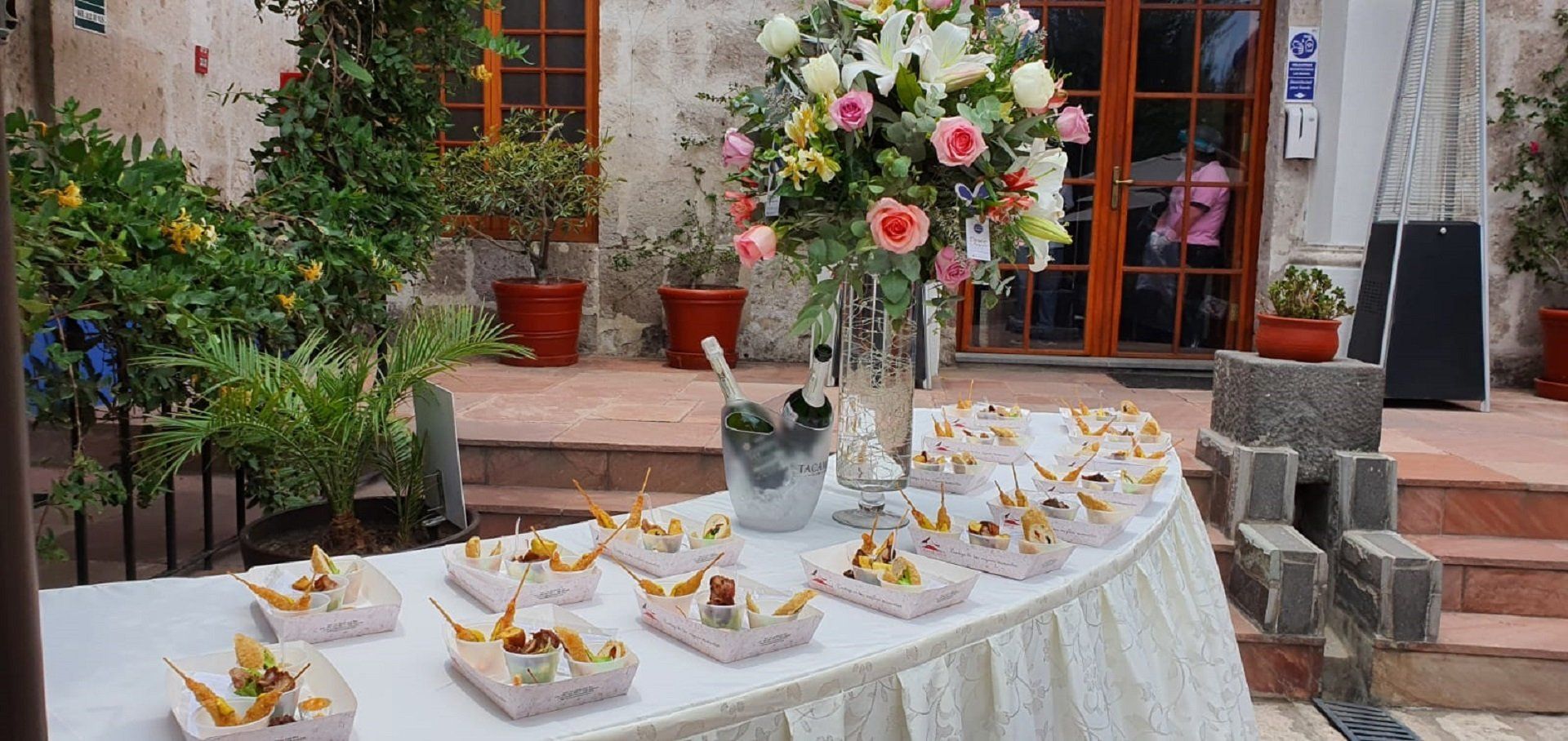 Outdoor dessert display on a white table with flower centerpieces in front of a building entrance