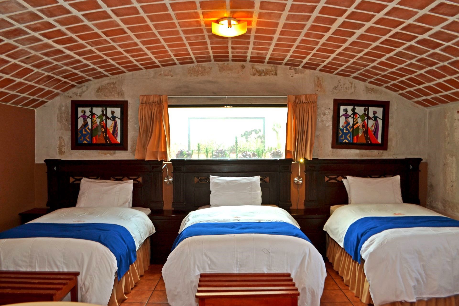 Three neatly made beds in a cozy room with a brick arched ceiling and a window in the center.