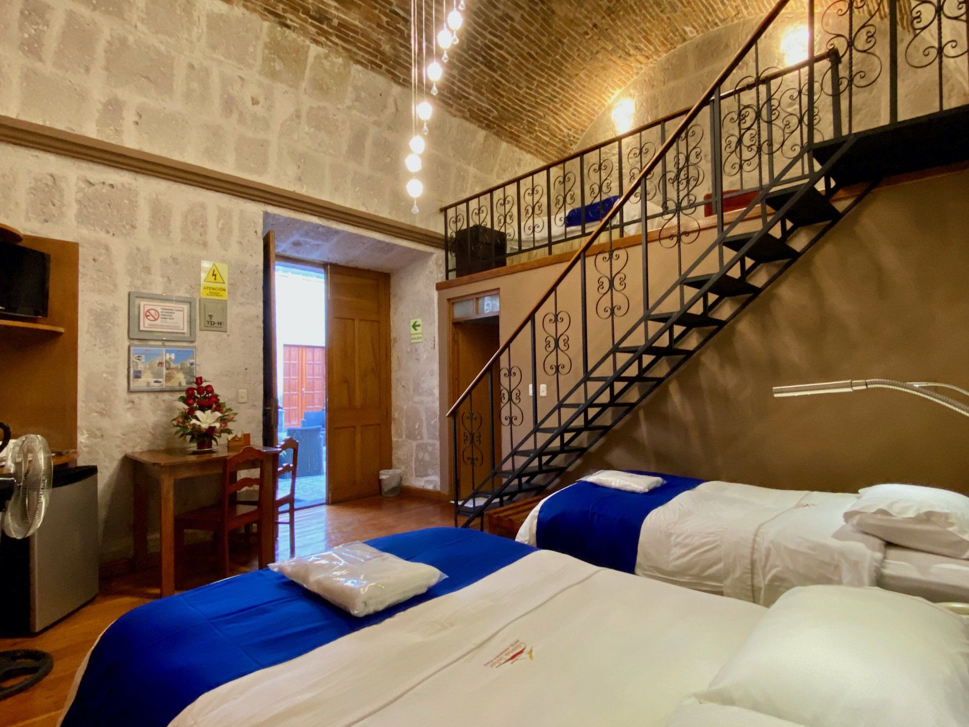 Loft bedroom with two twin beds, wrought-iron stairs, and a small desk under a vaulted brick ceiling