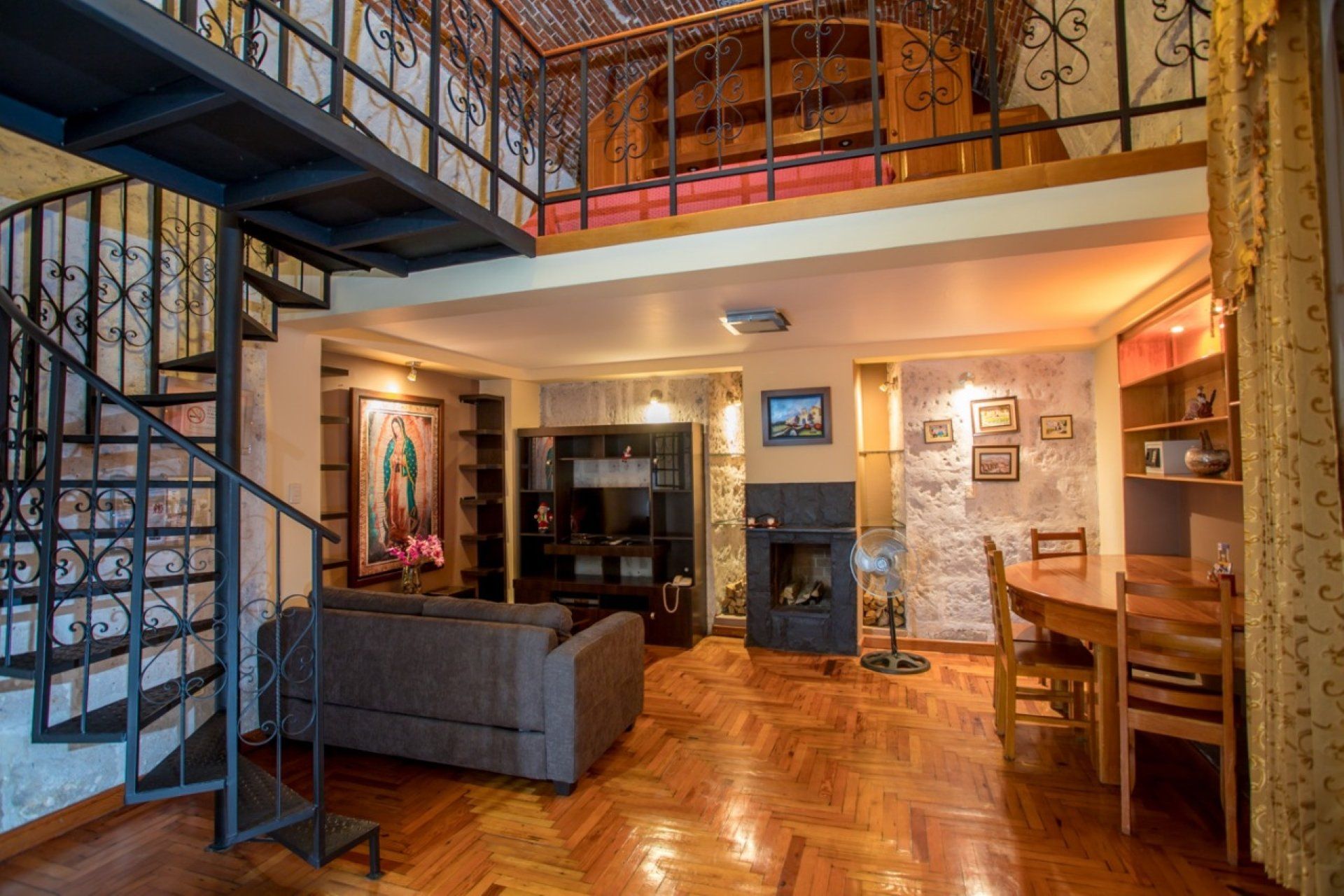 Loft living room with staircase, gray sofa, fireplace, wood floor, and dining area under mezzanine