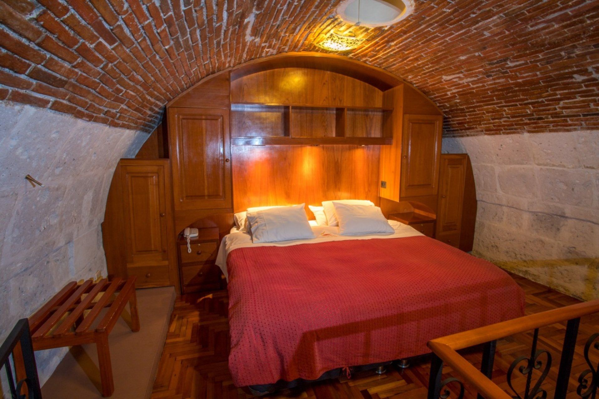 Cozy bedroom with arched brick ceiling, wooden walls, and a bed with red blanket and pillows.