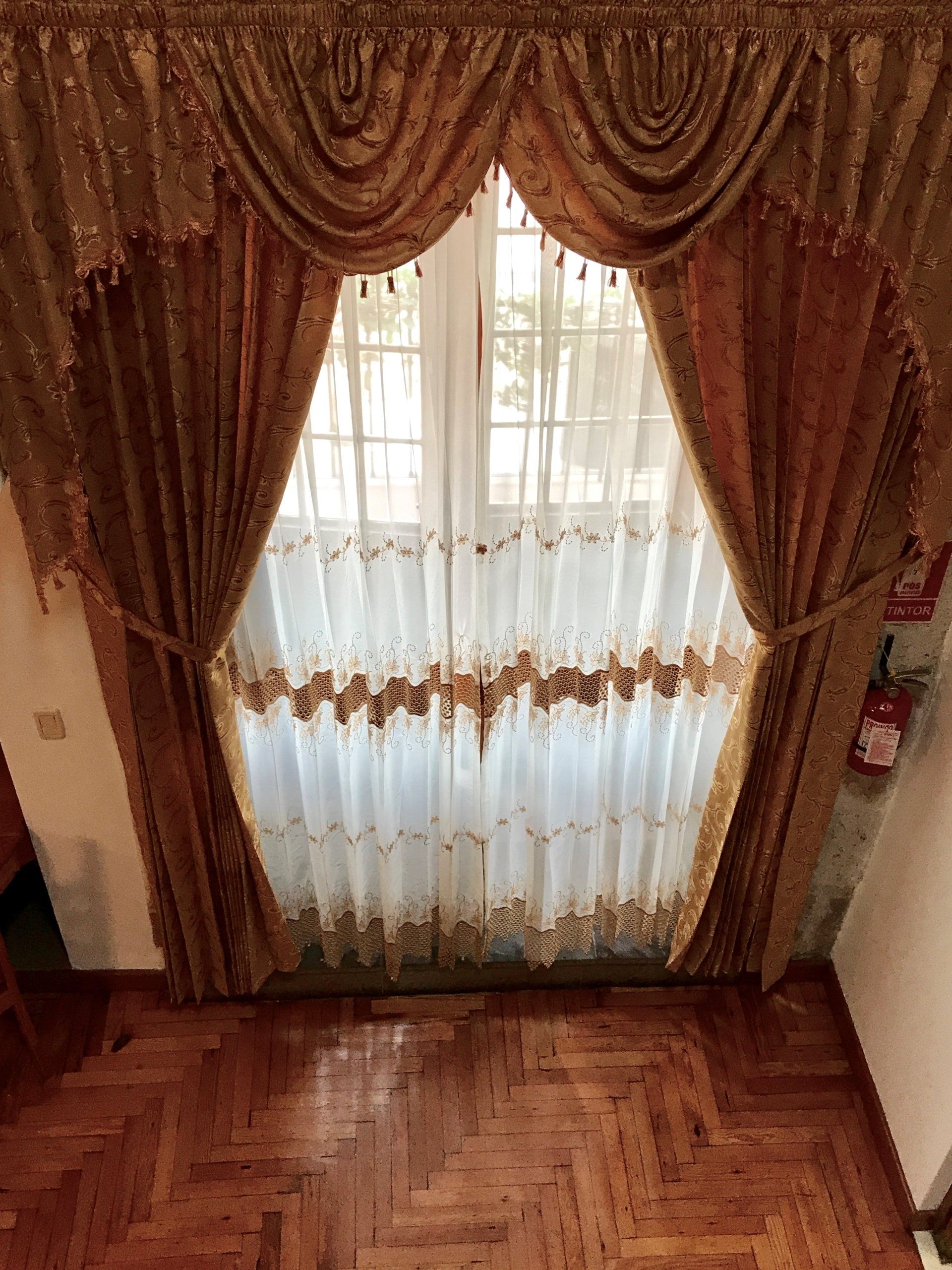 Decorative brown curtains framing a sheer white window over a parquet wood floor