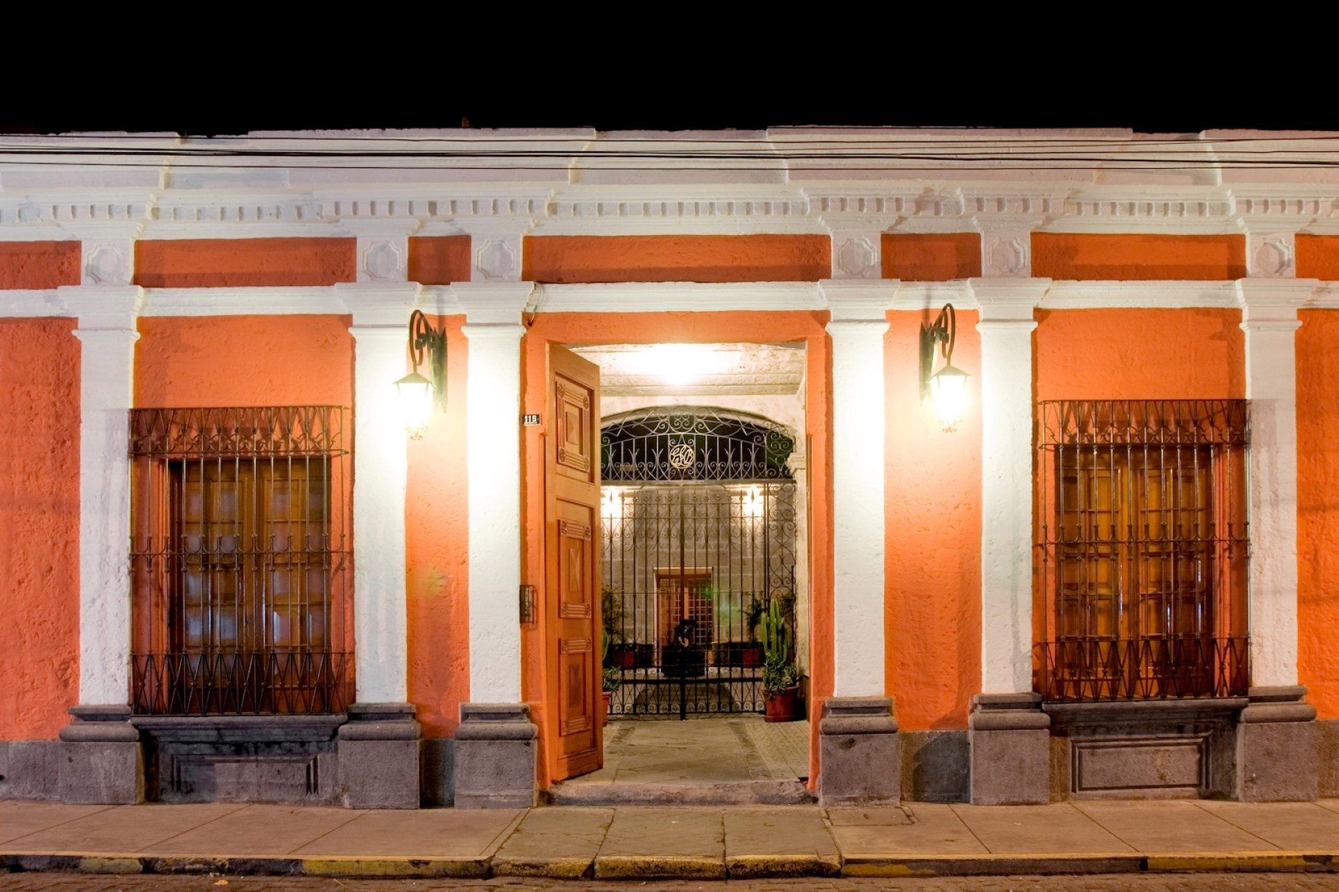 Exterior de un edificio con puerta abierta. El edificio es naranja con molduras blancas e iluminación interior.