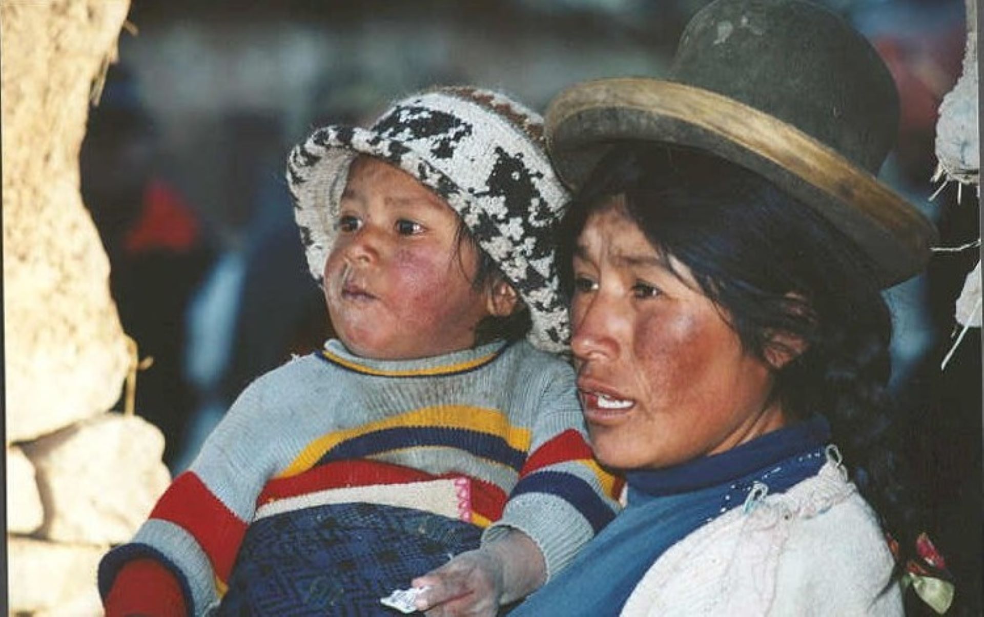 Adult holding a bundled child, both wearing hats, in an outdoor setting