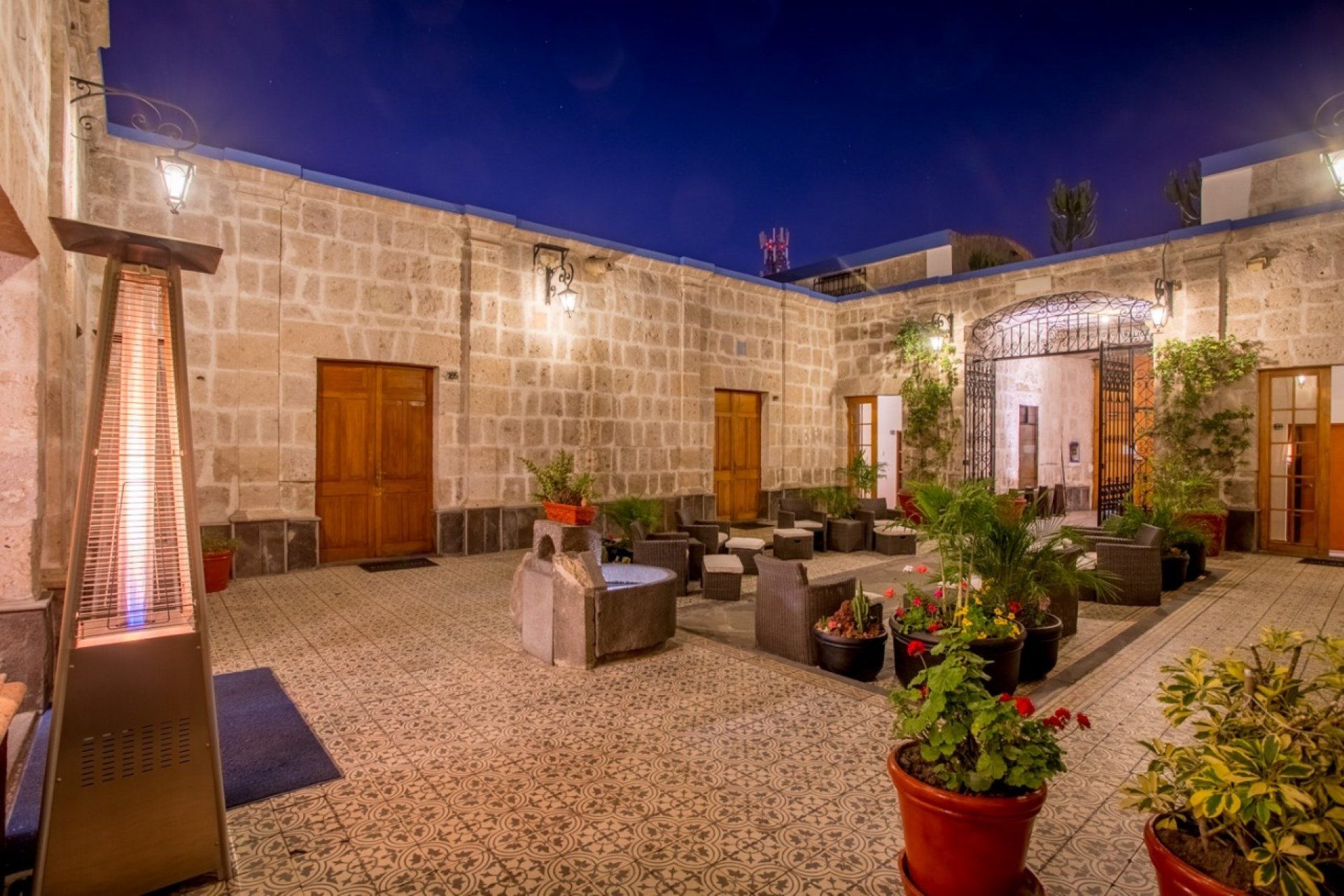 Stone courtyard patio with lounge chairs, potted plants, and warm lighting at dusk