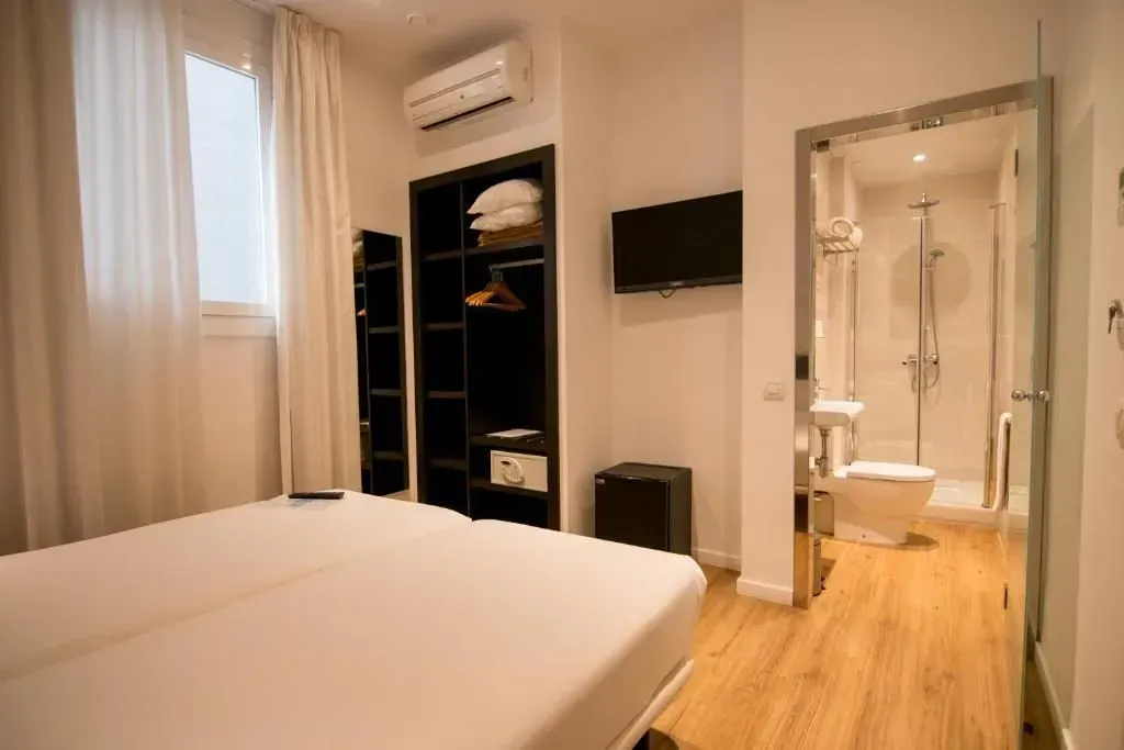 Una habitación de hotel con una cama, un armario abierto, un televisor montado en la pared, un aparato de aire acondicionado.