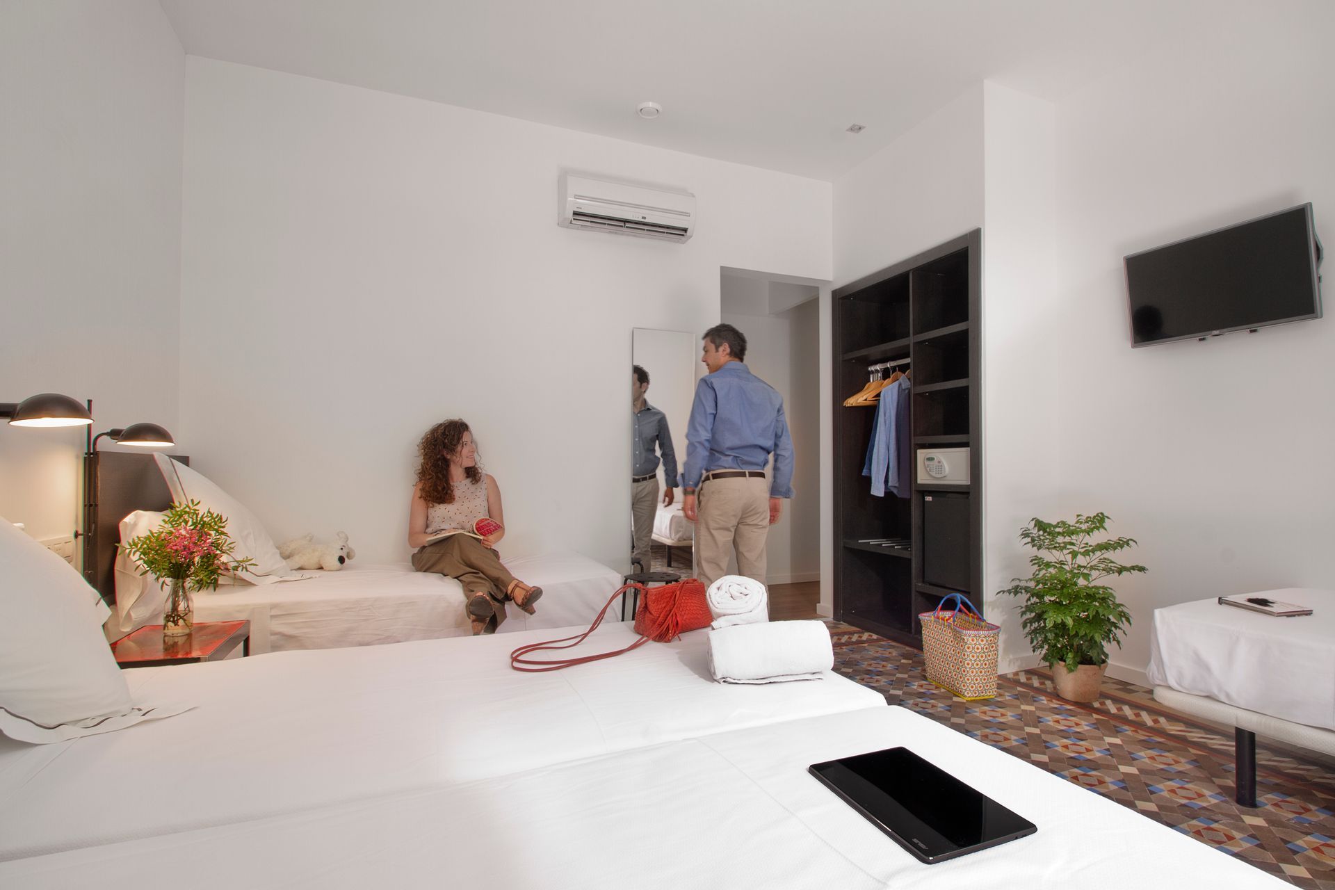 Luminoso salón con dos personas conversando cerca de un armario abierto y un televisor montado en la pared.