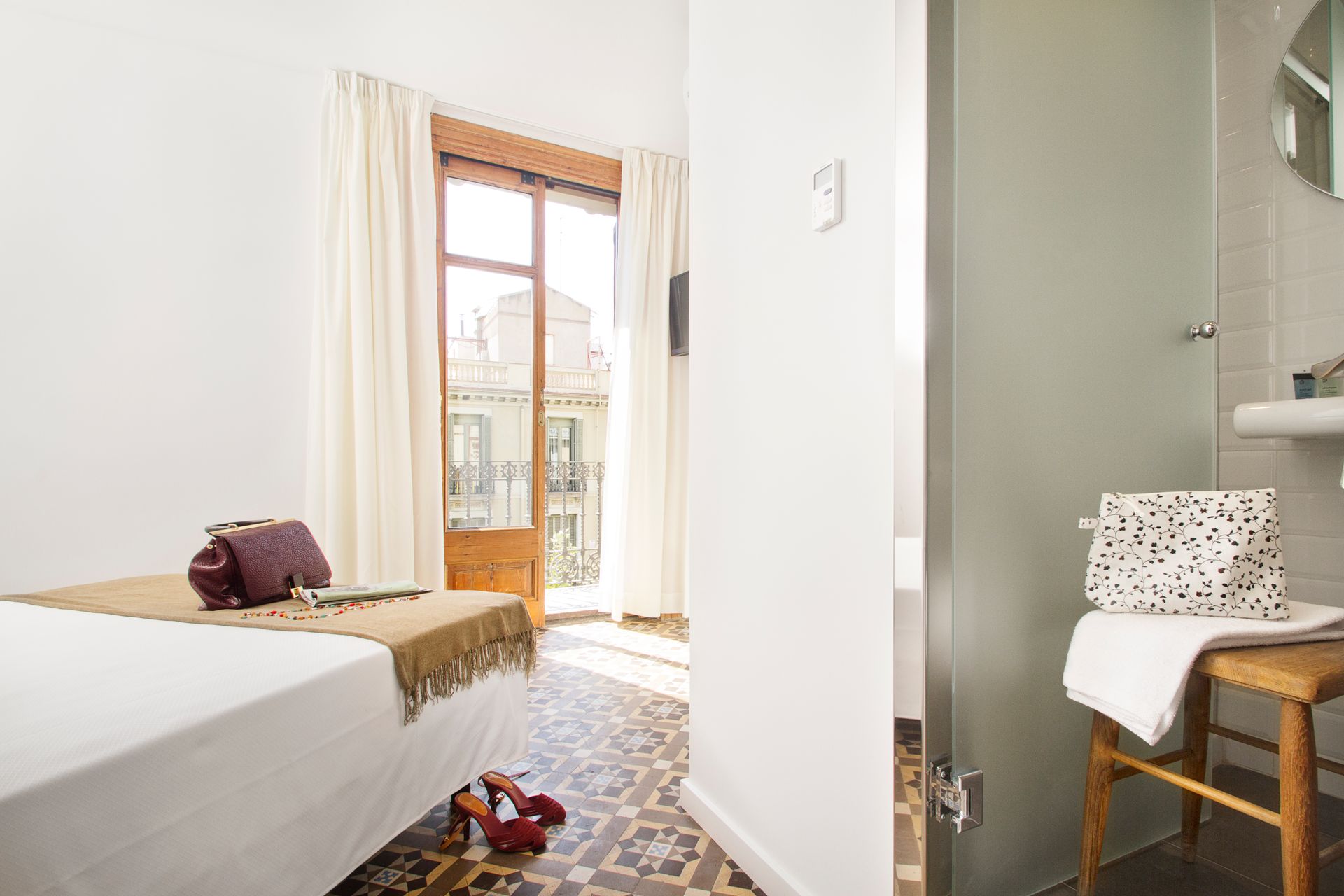 Habitación luminosa con dos camas individuales, puertas que dan al balcón y un pequeño tocador en el baño.