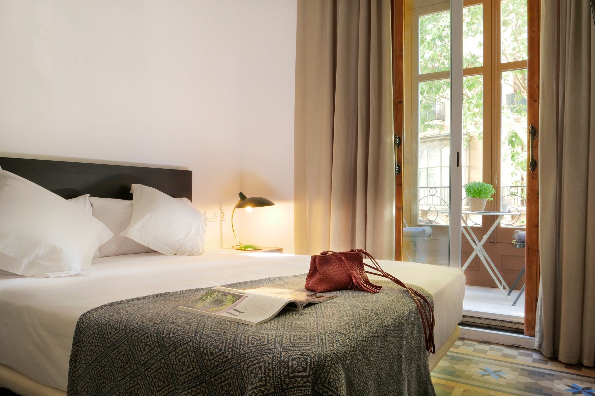 Habitación luminosa con una cama bien hecha, lámpara de noche y puerta que da a un pequeño patio.