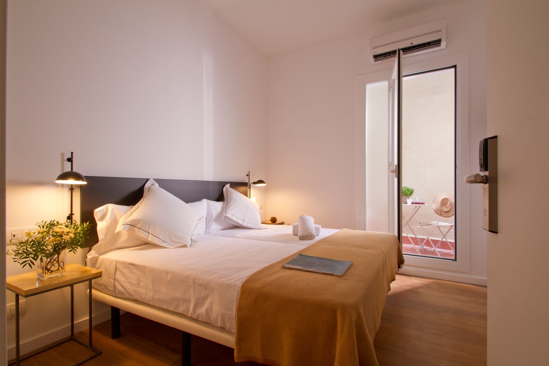 Habitación luminosa con una cama bien hecha, lámparas de noche y una puerta que da a un pequeño patio.