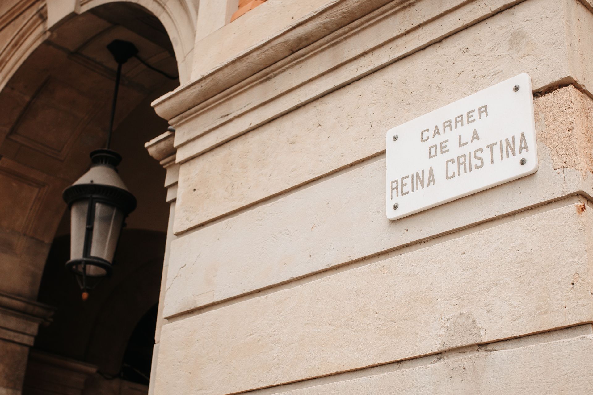 Letrero de calle con las inscripciones “Carre...” y “Reina Cristina” en la esquina de un edificio de piedra.