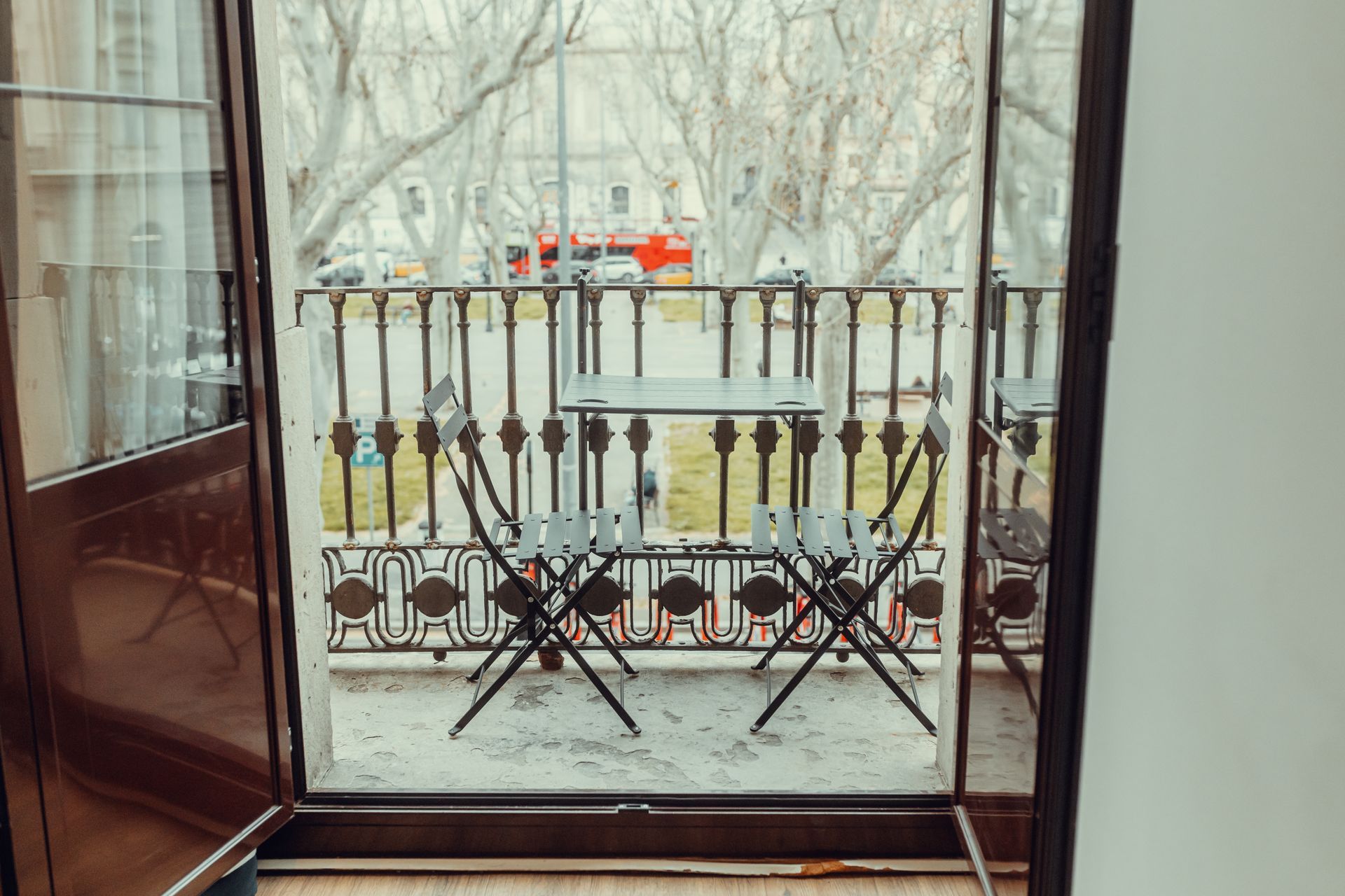 Balcón con barandilla ornamentada, dos sillas de patio negras y árboles nevados más allá de la puerta de cristal.