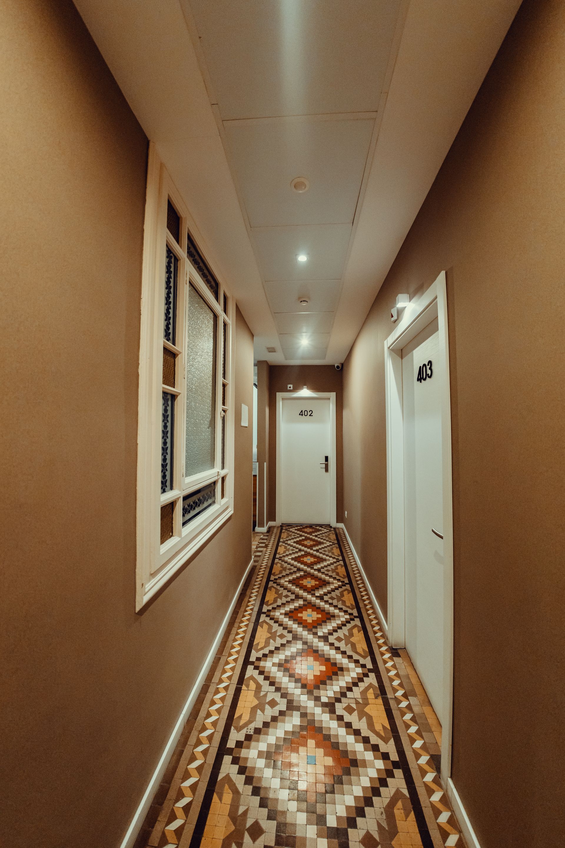 Pasillo estrecho con alfombra estampada, paredes beige, puertas blancas y luces empotradas en el techo.