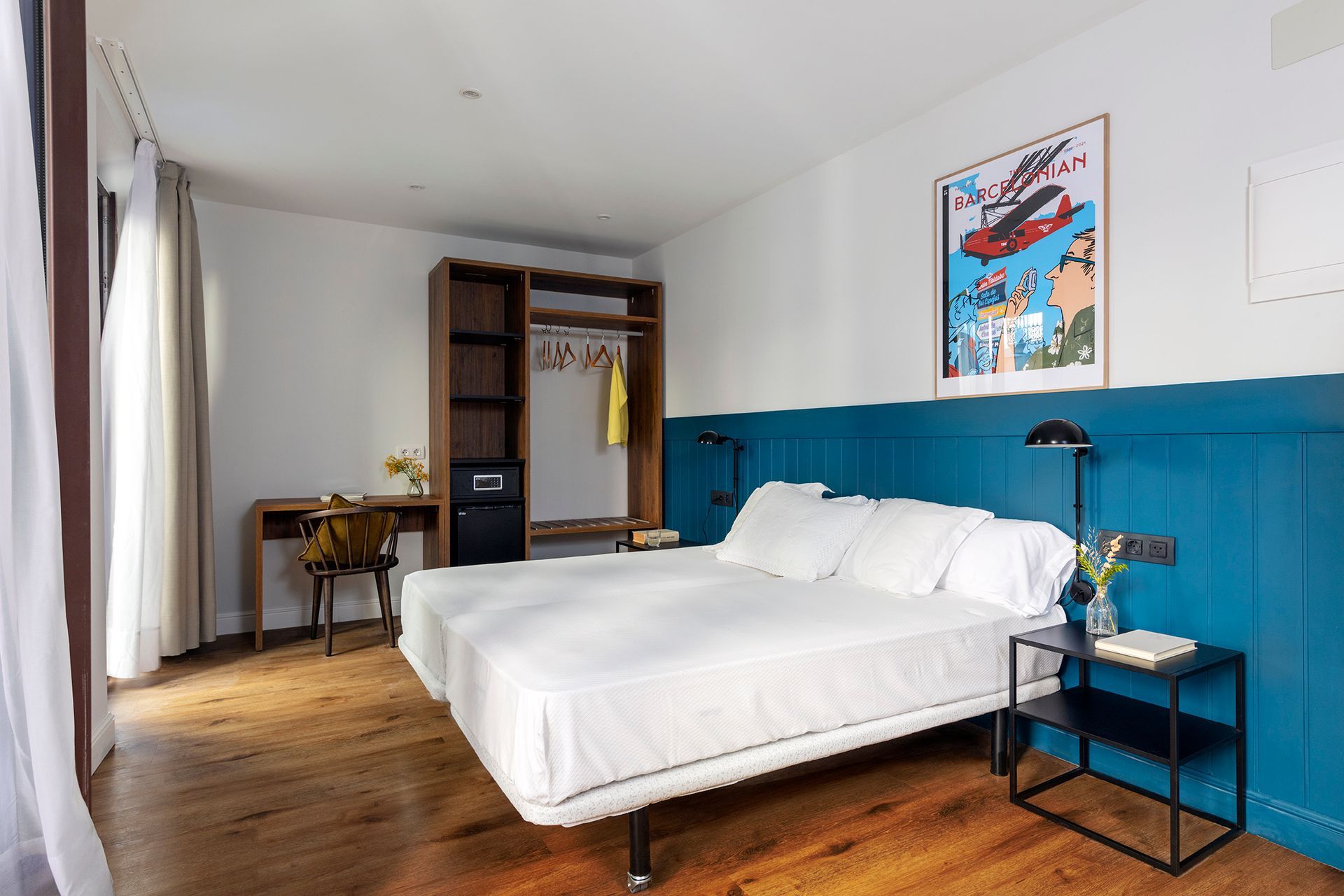 Dormitorio moderno con cama blanca, pared decorativa color turquesa, suelo de madera, escritorio y armario.