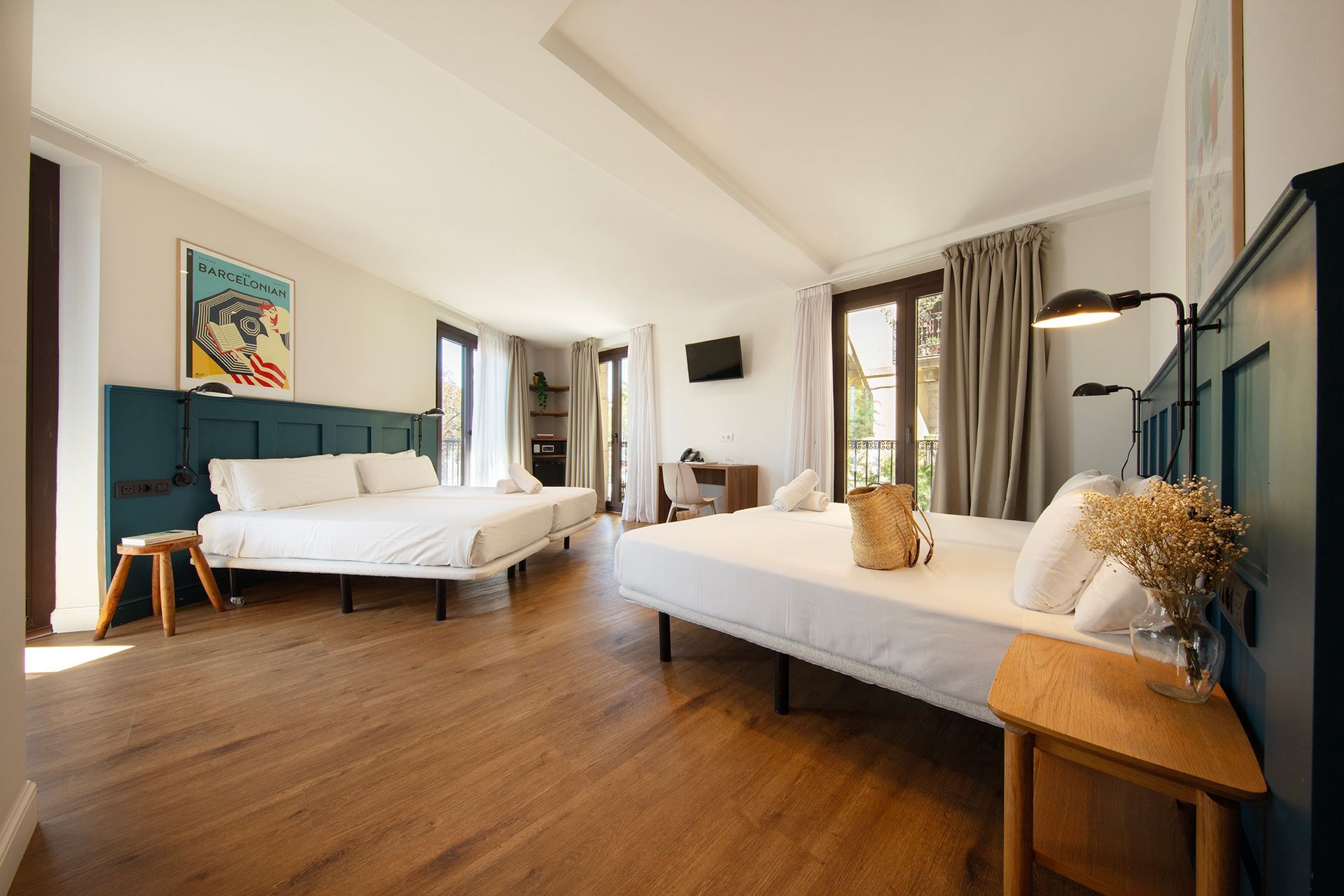 Habitación de hotel luminosa con dos camas, suelos de madera, detalles en color turquesa y grandes ventanales.