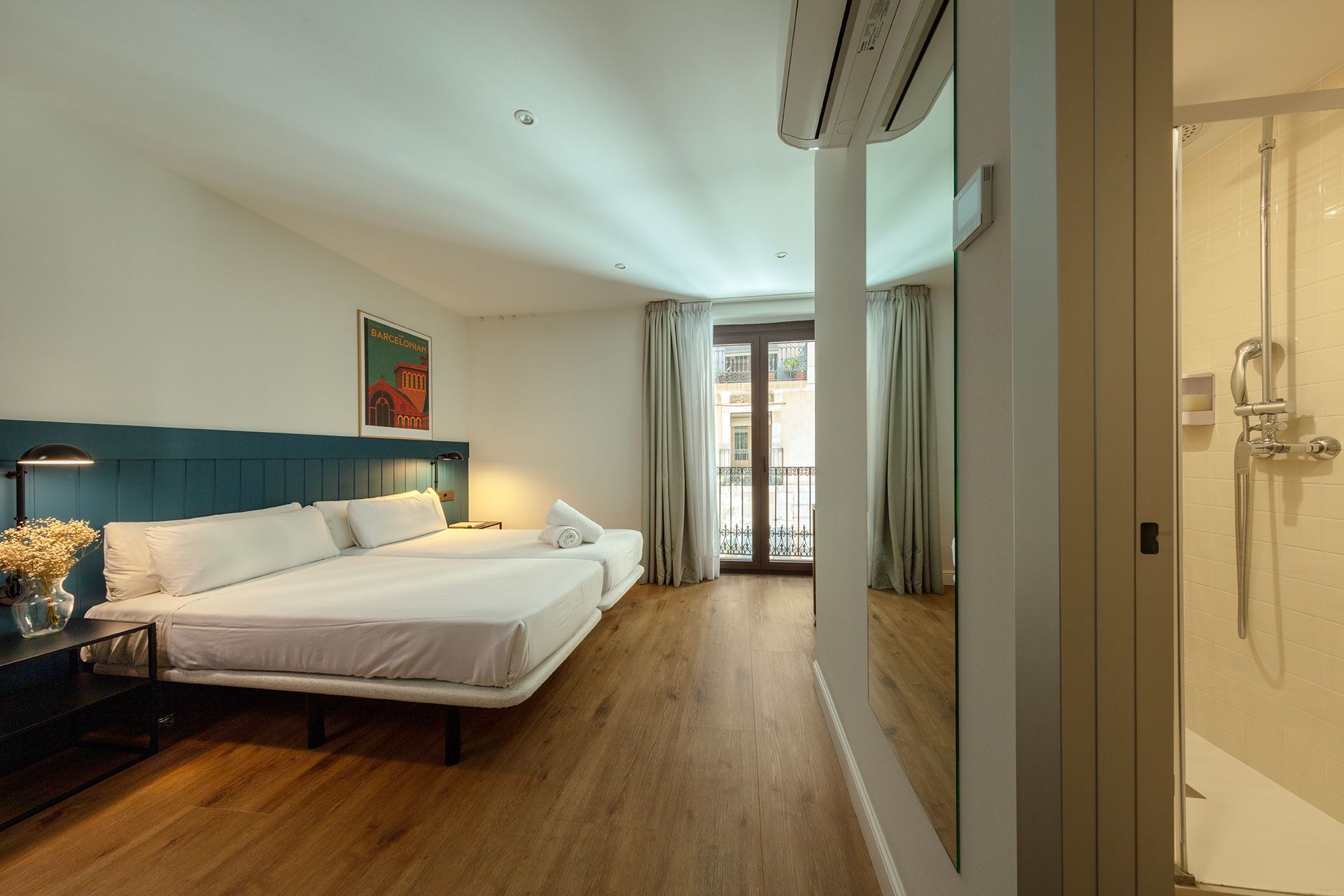 Dormitorio moderno con cabecero color turquesa, cama grande, suelo de madera y puerta de baño de cristal al lado.