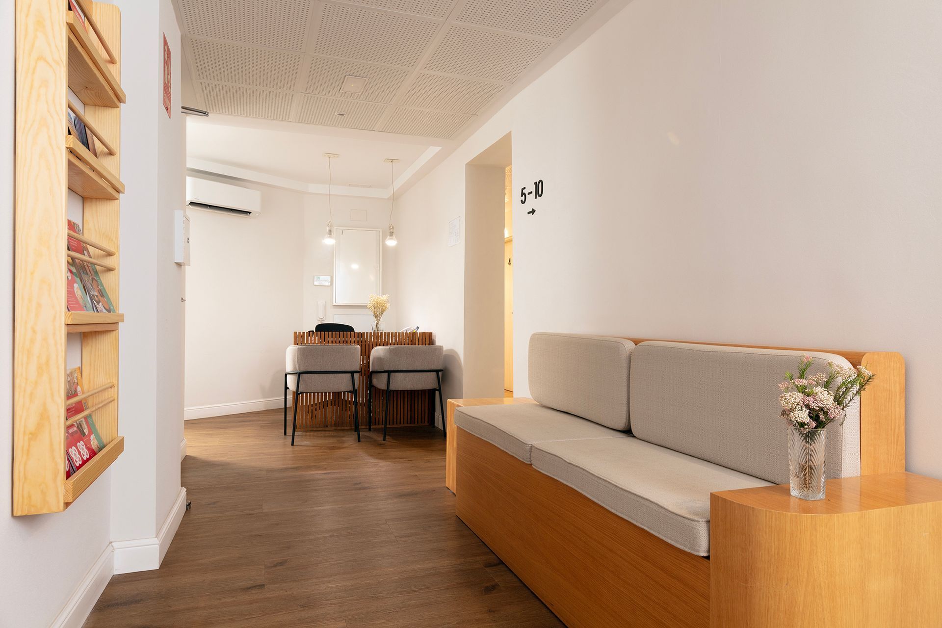 Pasillo estrecho con suelo de madera, sofá beige, mesa de comedor pequeña y obras de arte en la pared en un luminoso interior