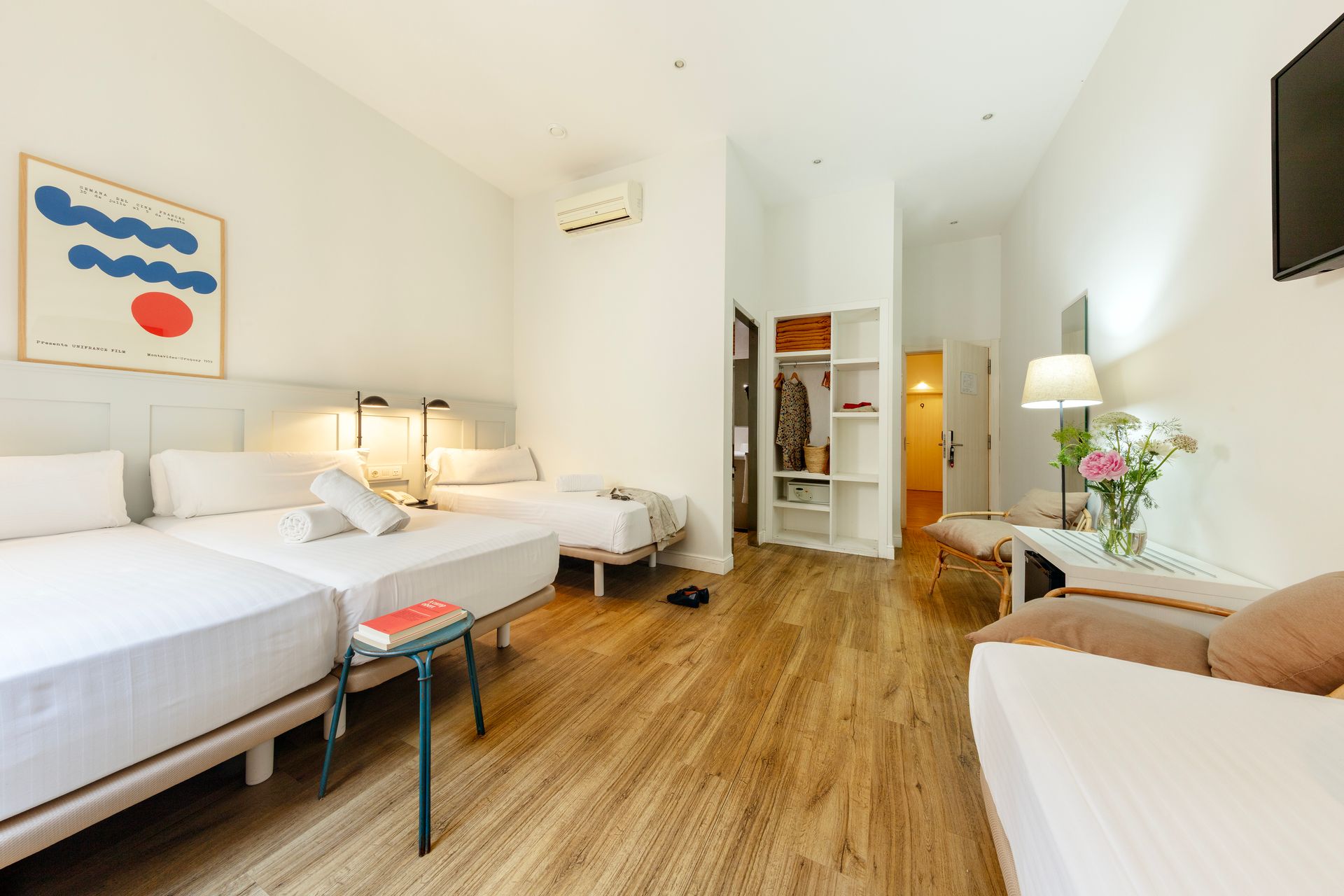 Habitación luminosa con dos camas individuales, suelo de madera y una acogedora zona de estar junto a la ventana.