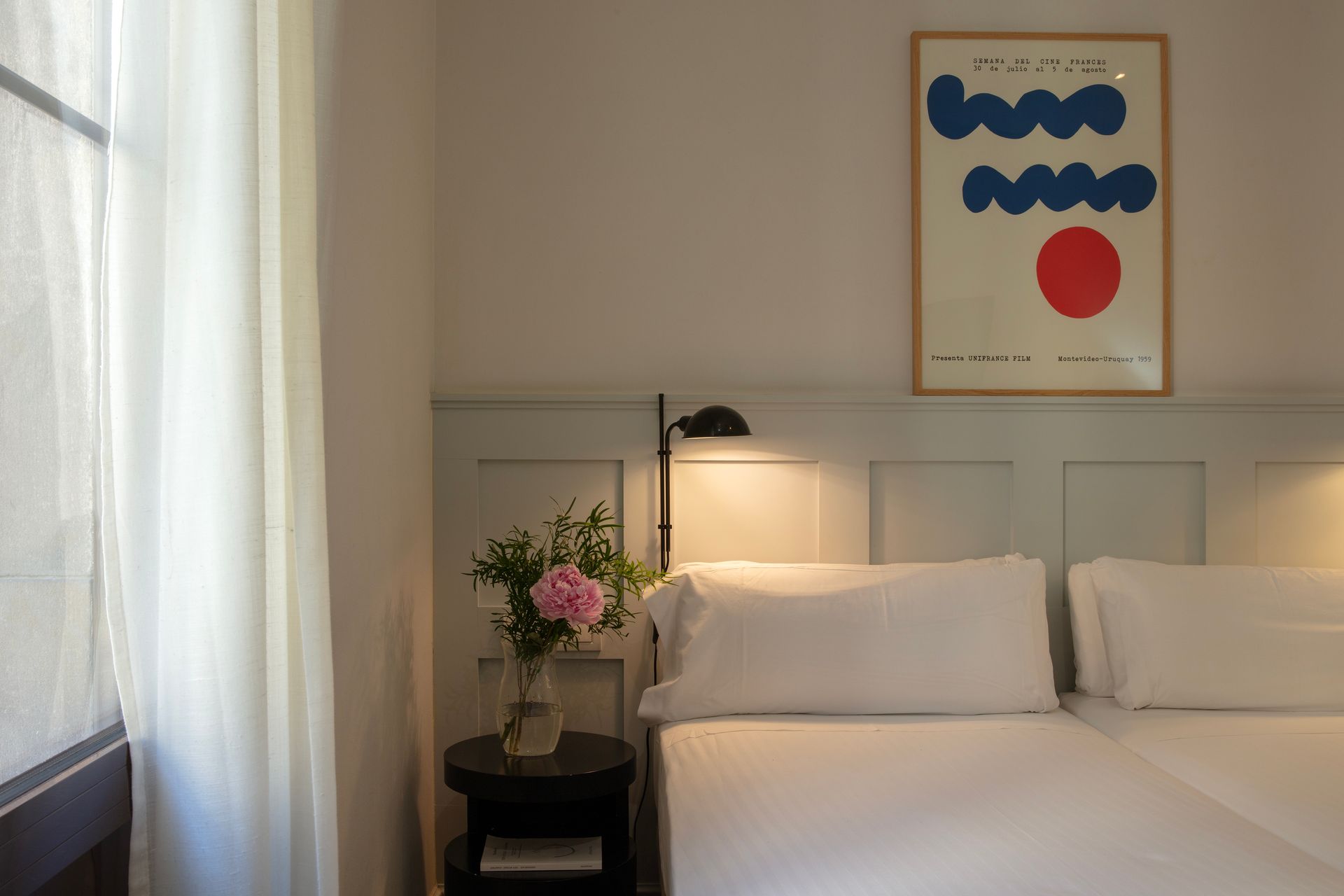 Habitación acogedora con cama, lámpara de noche, jarrón con flores y arte abstracto en la pared junto a la ventana.