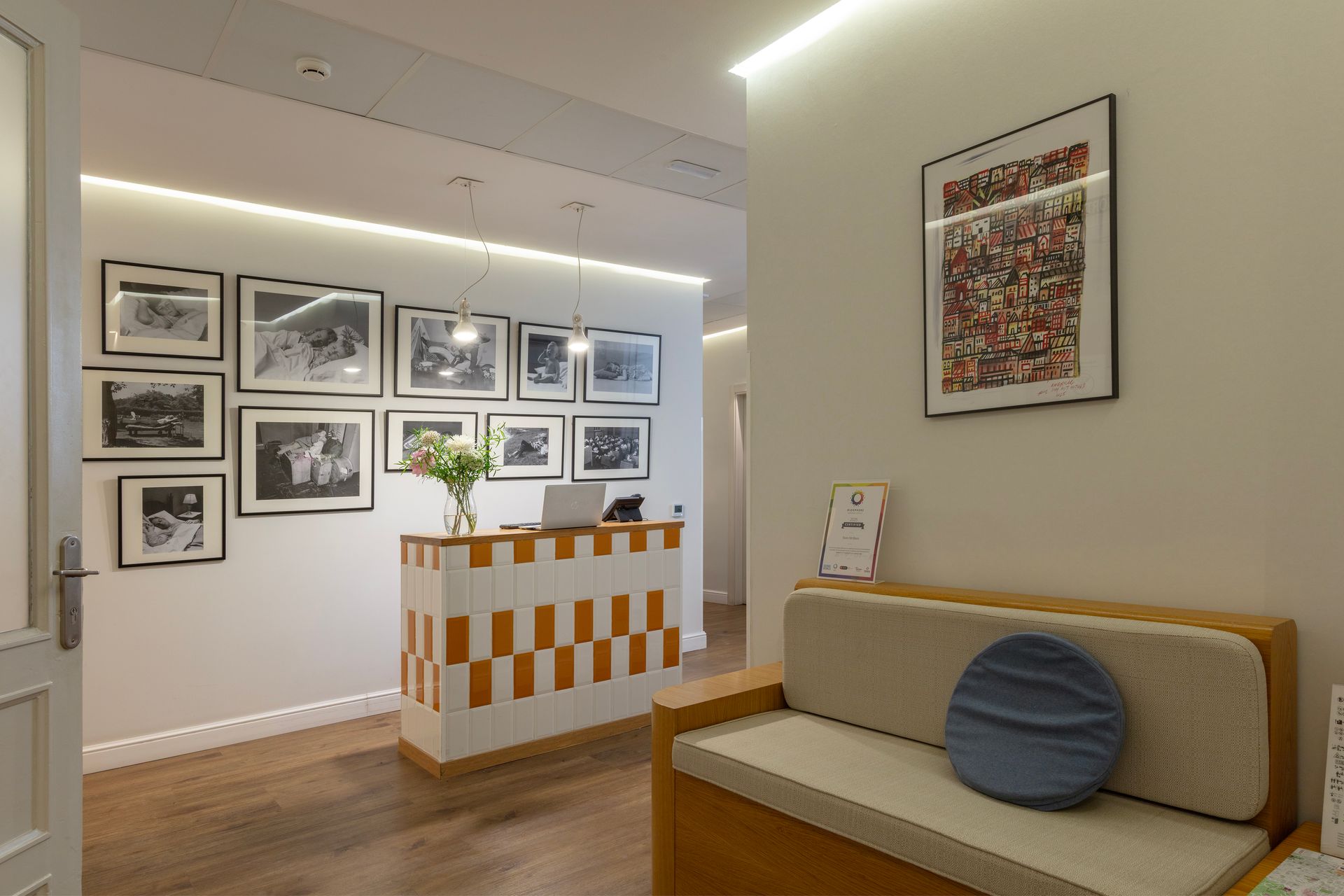 Vestíbulo moderno con aspecto de galería de arte, con cuadros enmarcados en paredes blancas y un banco beige.
