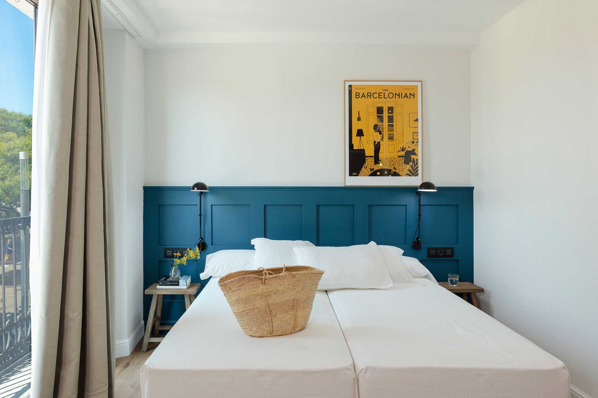Habitación luminosa con cabecero azul, ropa de cama blanca y una cesta de mimbre sobre la cama.