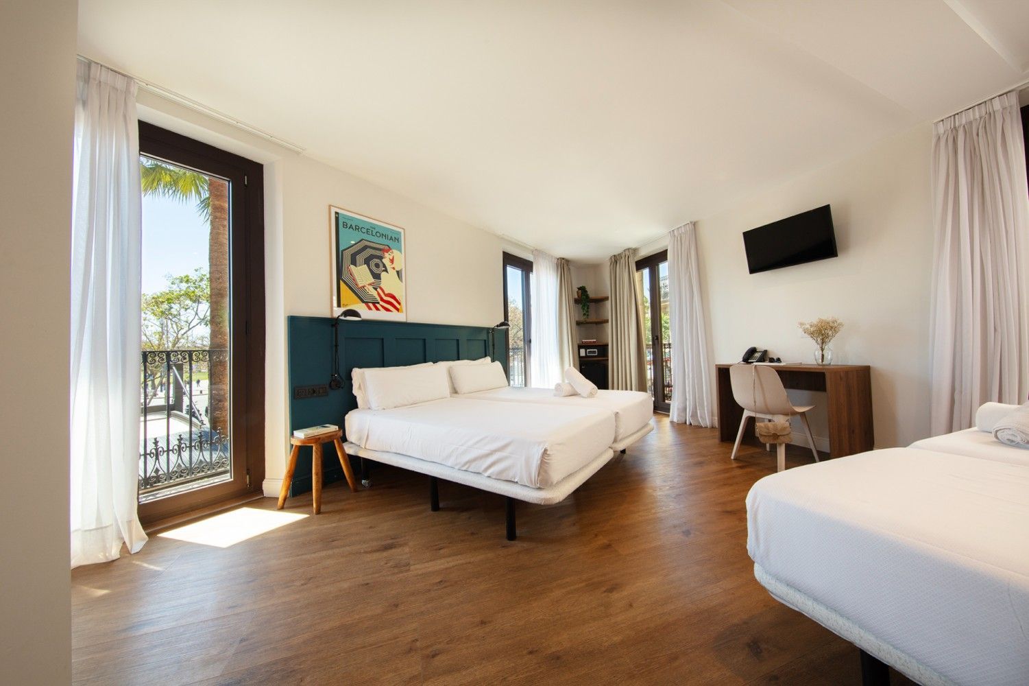 Una luminosa habitación de hotel con suelos de madera, dos camas blancas, un escritorio de madera con silla.