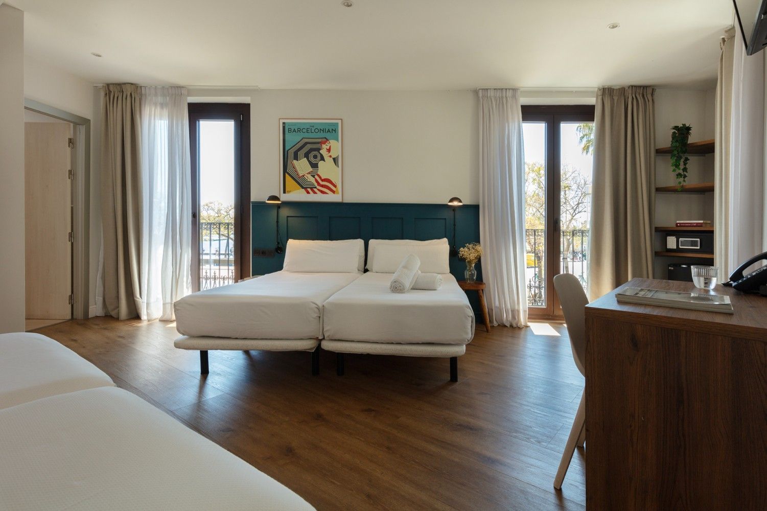 Una habitación de hotel con dos camas individuales juntas, piso de madera oscura, cortinas claras.
