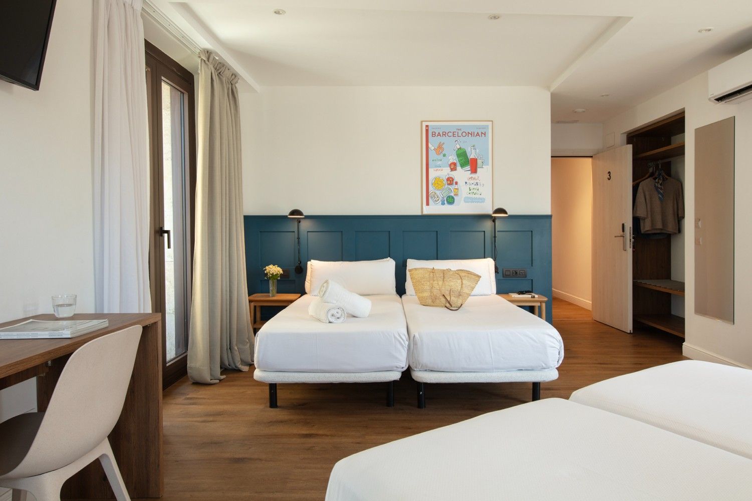 Una habitación de hotel con dos camas individuales con sábanas blancas sobre una pared verde azulado oscuro.