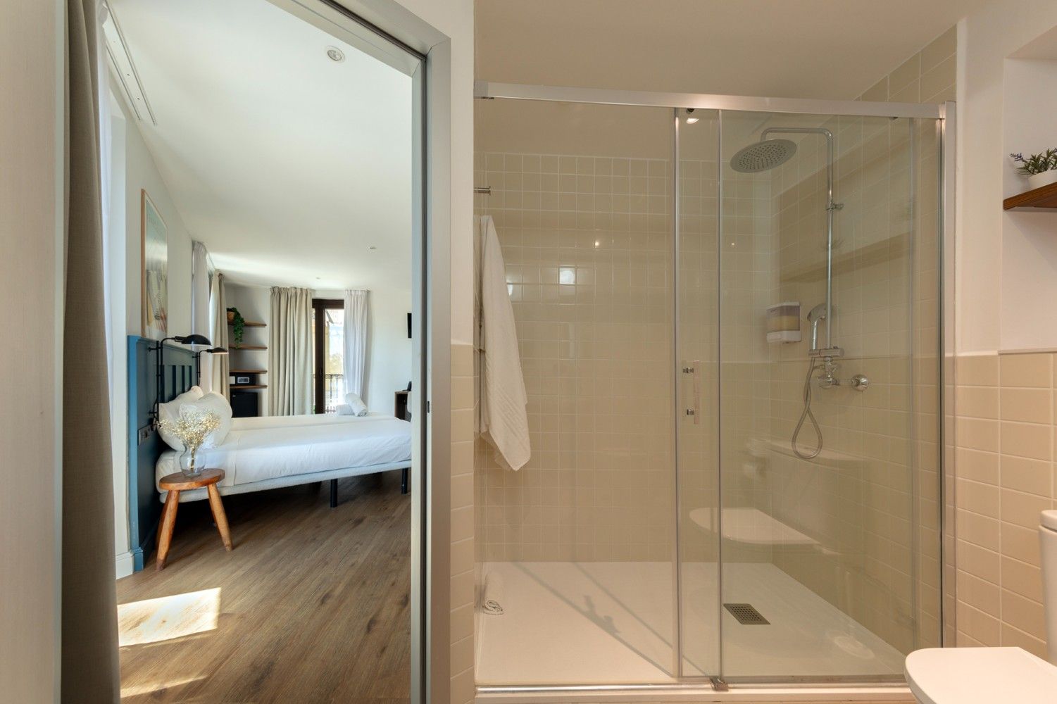 Un baño con cabina de ducha con mampara de cristal, con vista a través de una puerta abierta a un dormitorio .