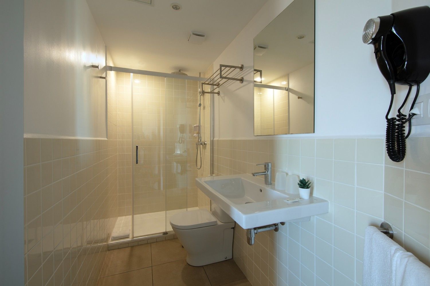 Baño pequeño y moderno con ducha, inodoro, lavabo y secador de pelo de pared.