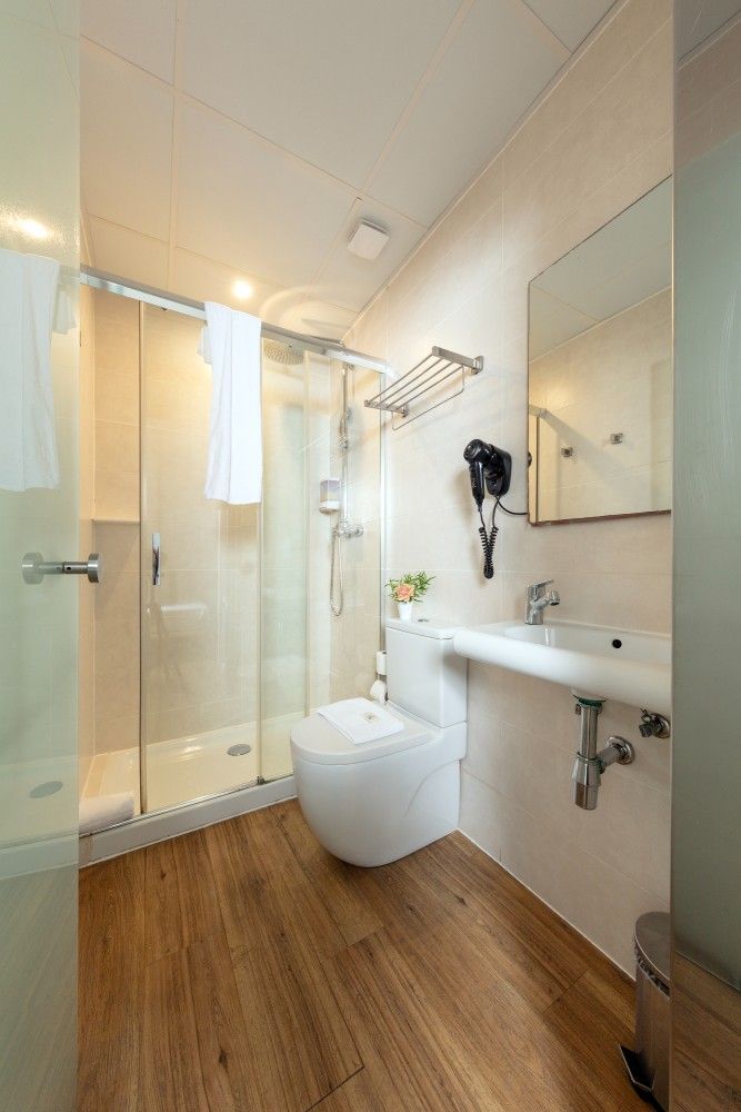 Un baño moderno con ducha con mampara de cristal, inodoro blanco y lavabo con espejo de pared.