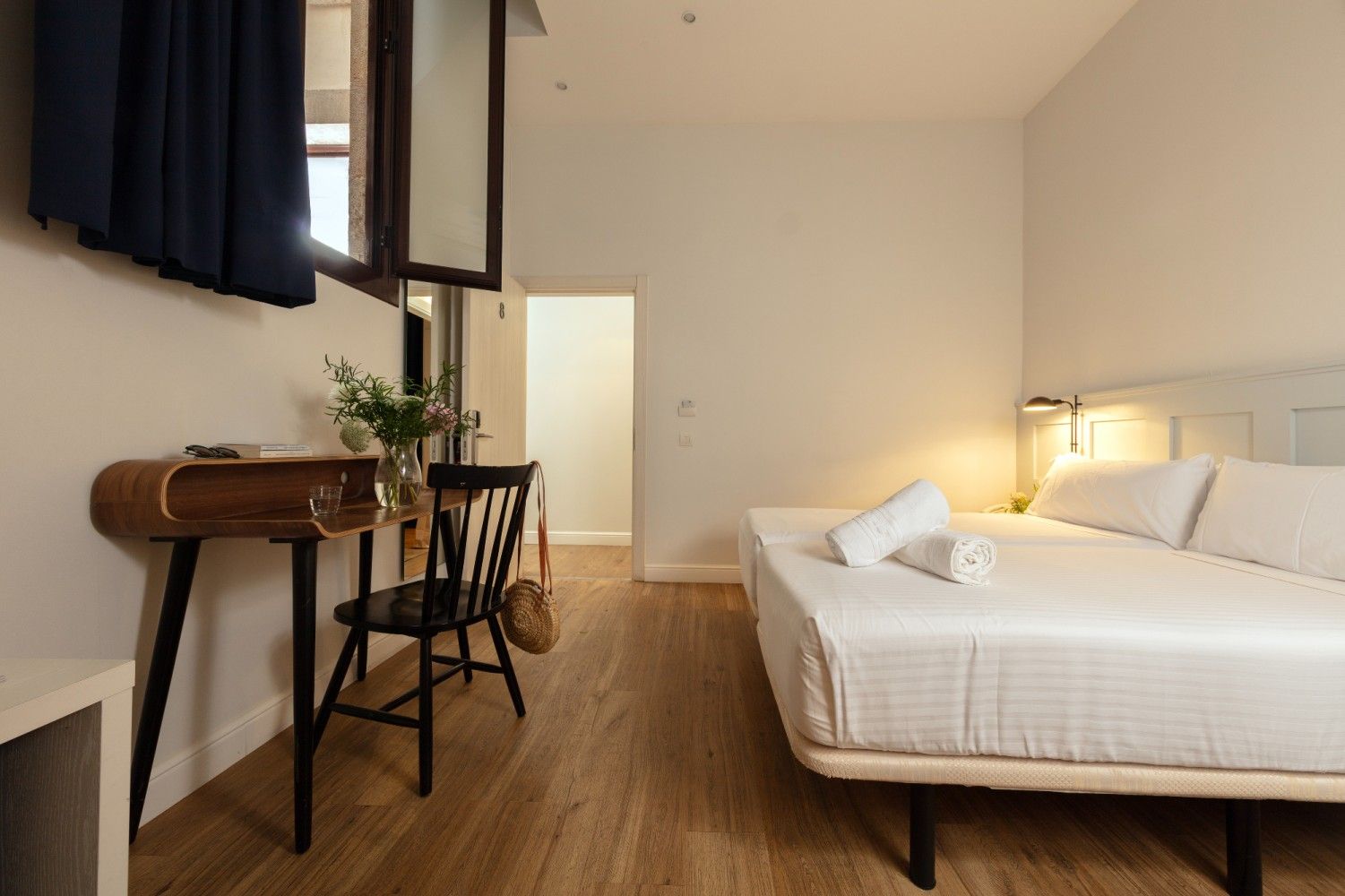 Un dormitorio minimalista con una cama grande, un escritorio de madera con una silla negra y pisos de madera clara.