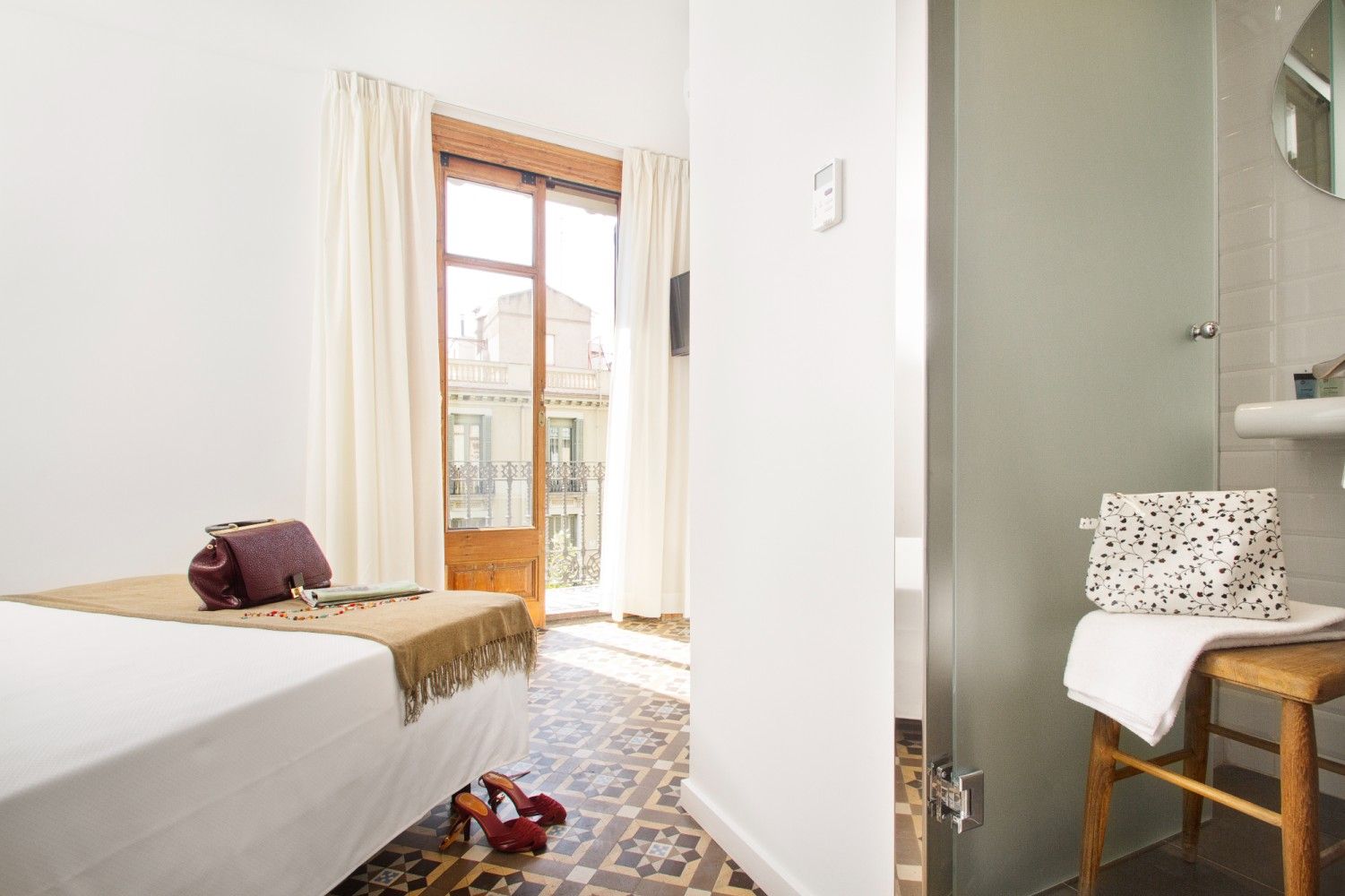 Habitación luminosa con cama, puertas que dan al balcón, silla de escritorio y alfombra estampada.