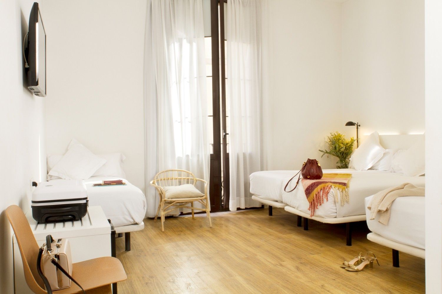 Una luminosa habitación de hotel con una cama individual, dos camas individuales, una pequeña silla de ratán.