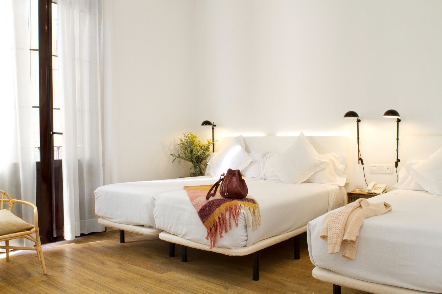 Habitación de hotel luminosa con dos camas blancas, lámparas de lectura junto a la cama.